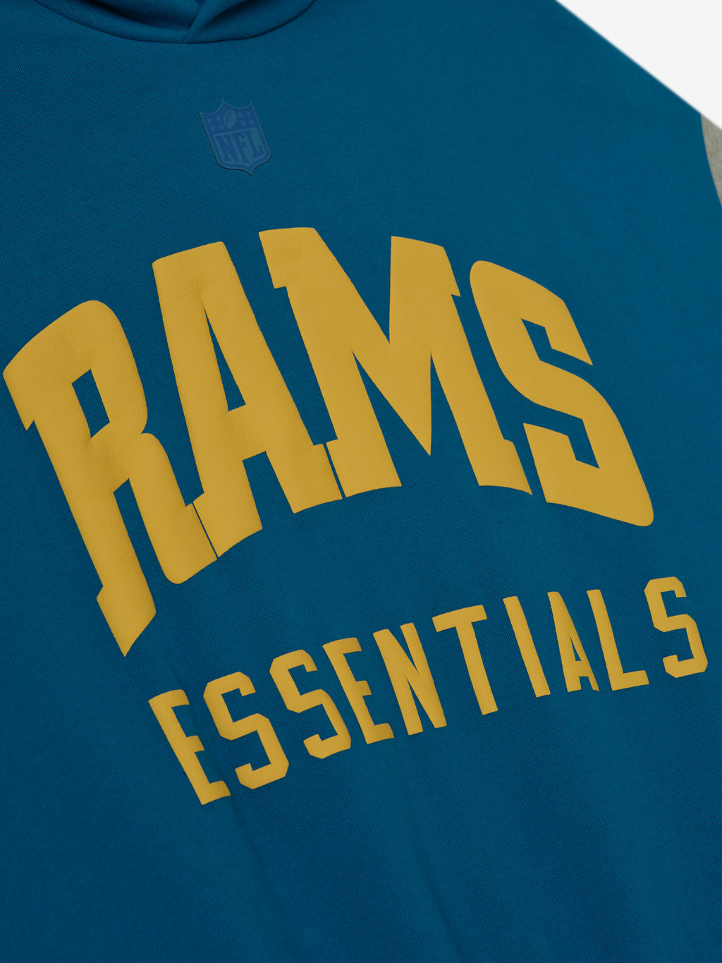 Close-up of blue sapphire Rams Sport Hoodie showing bold gold Rams Essentials text and subtle NFL logo above the chest