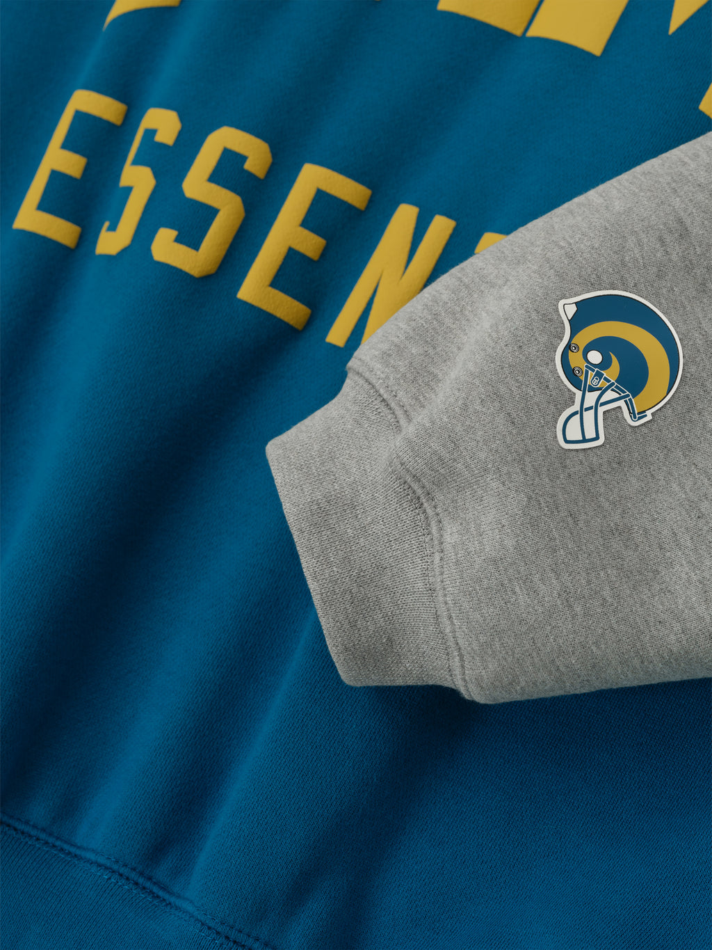 Close-up of Rams Sport Hoodie showing blue sapphire body, gold Essentials text, and concrete heather sleeve with Rams helmet patch