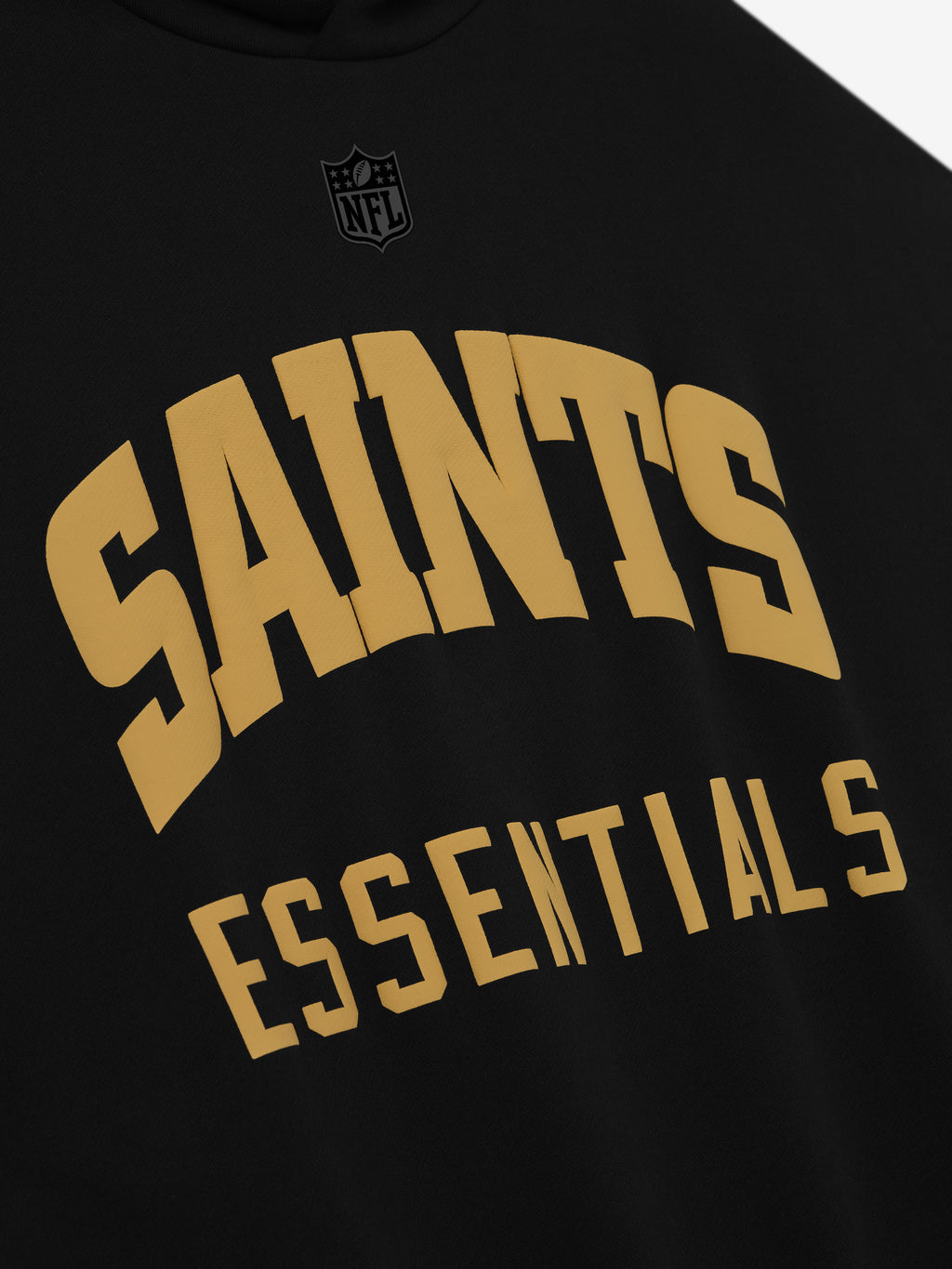 Close-up of black Saints Sport Hoodie front showing gold Saints Essentials text and subtle black NFL logo above