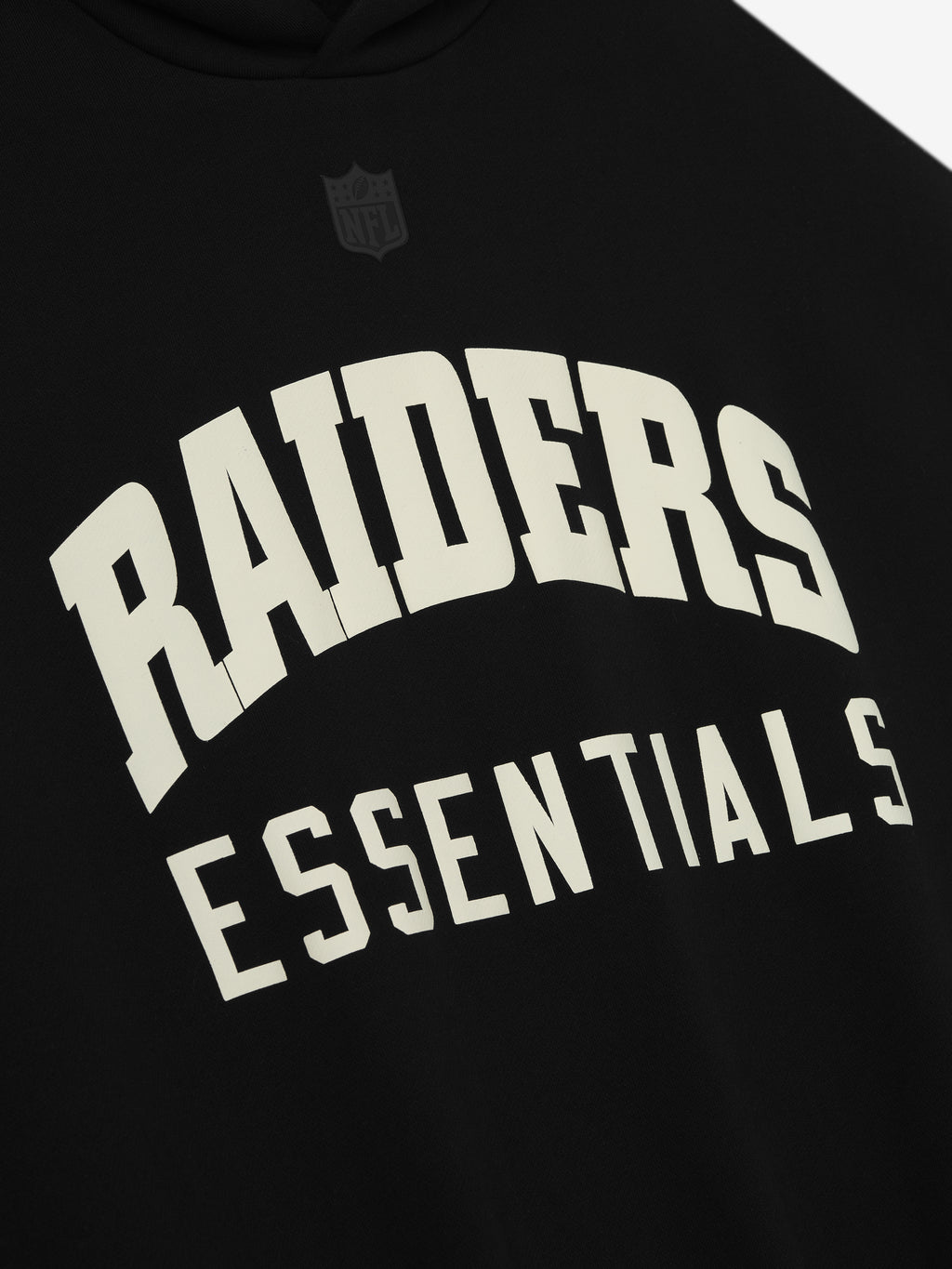 Close-up of black Raiders Sport Hoodie front showing large white Raiders Essentials text with subtle black NFL logo above