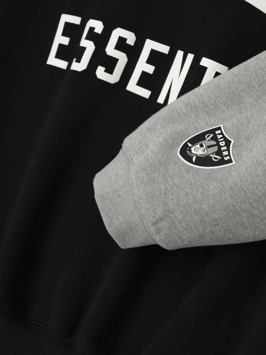 Close-up of Raiders Sport Hoodie showing concrete heather sleeve with team logo and black body with partial Essentials text