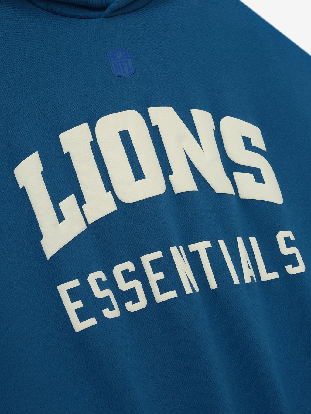 Close-up of blue sapphire Lions Sport Hoodie front showing large white Lions Essentials text and subtle tone-on-tone NFL logo above