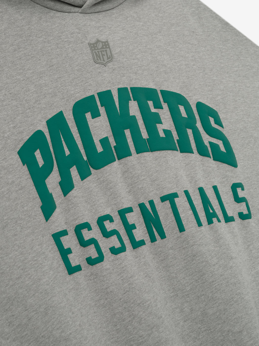 Close-up of Packers Sport Hoodie front in concrete heather showing green Packers Essentials text and faint NFL logo above