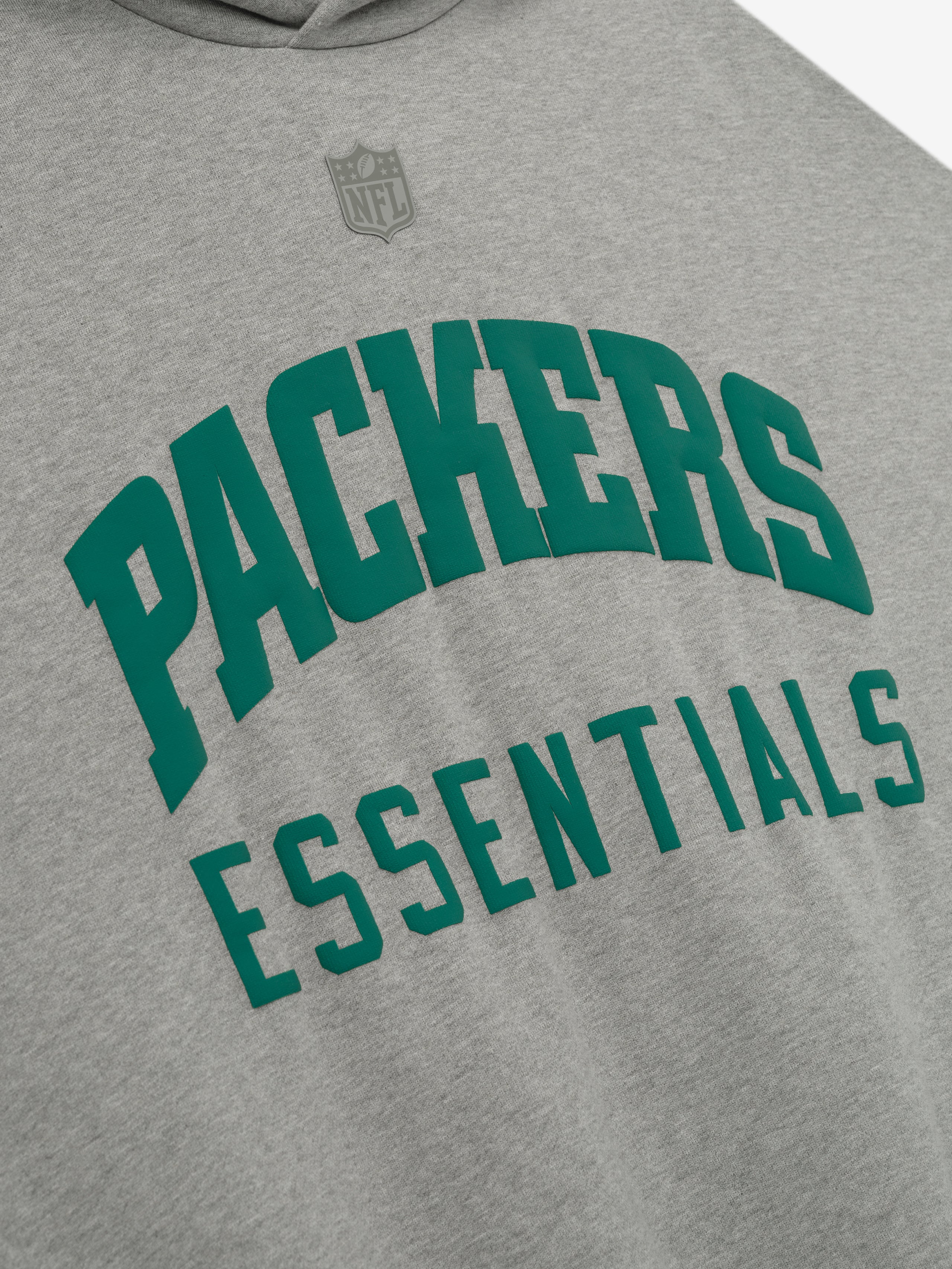 Close-up of Packers Sport Hoodie front in concrete heather showing green Packers Essentials text and faint NFL logo above