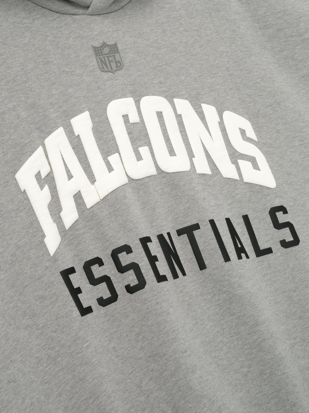 Close-up of Falcons Sport Hoodie in concrete heather showing white Falcons and black Essentials text with subtle gray NFL shield above