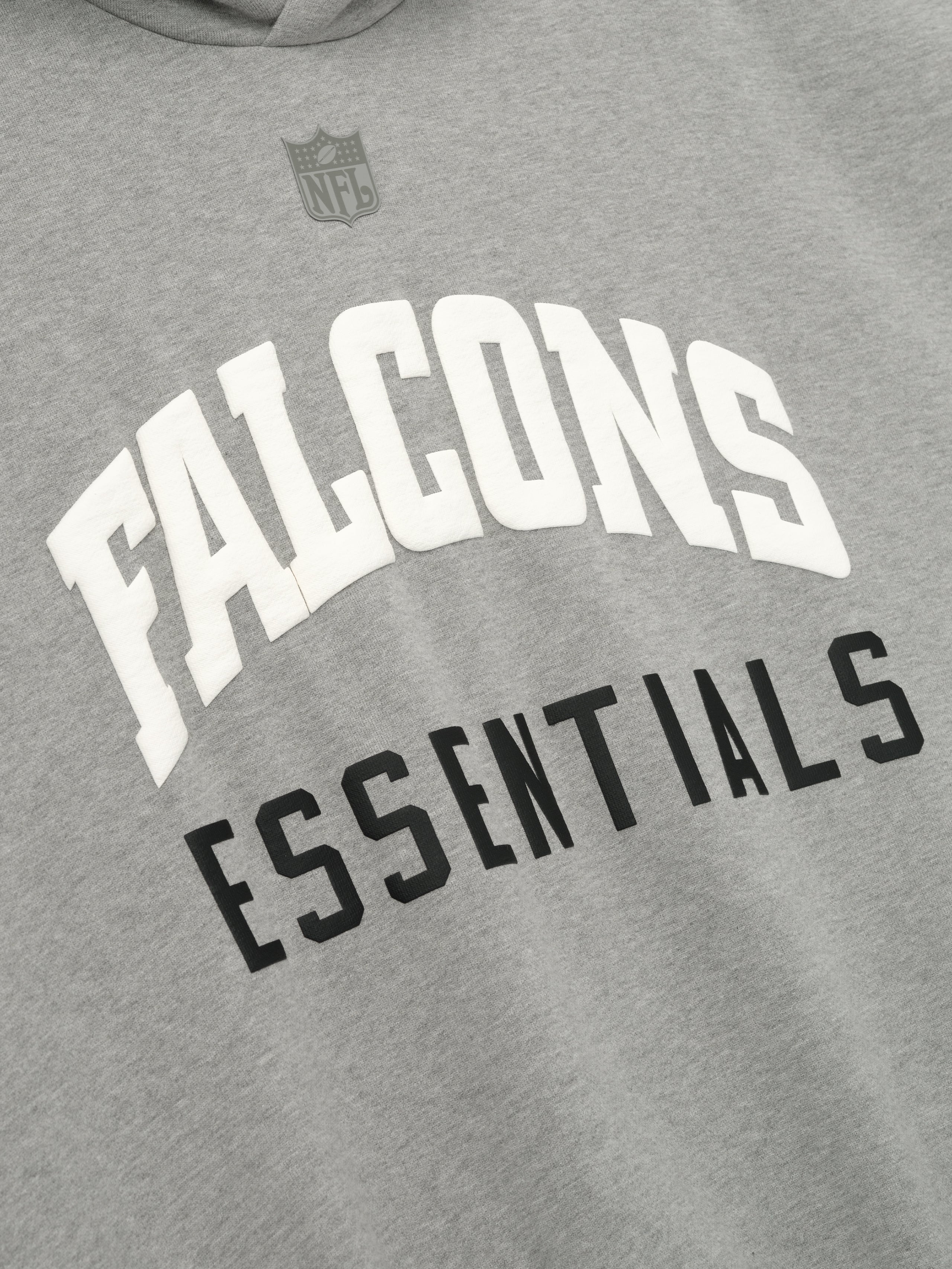 Close-up of Falcons Sport Hoodie in concrete heather showing white Falcons and black Essentials text with subtle gray NFL shield above
