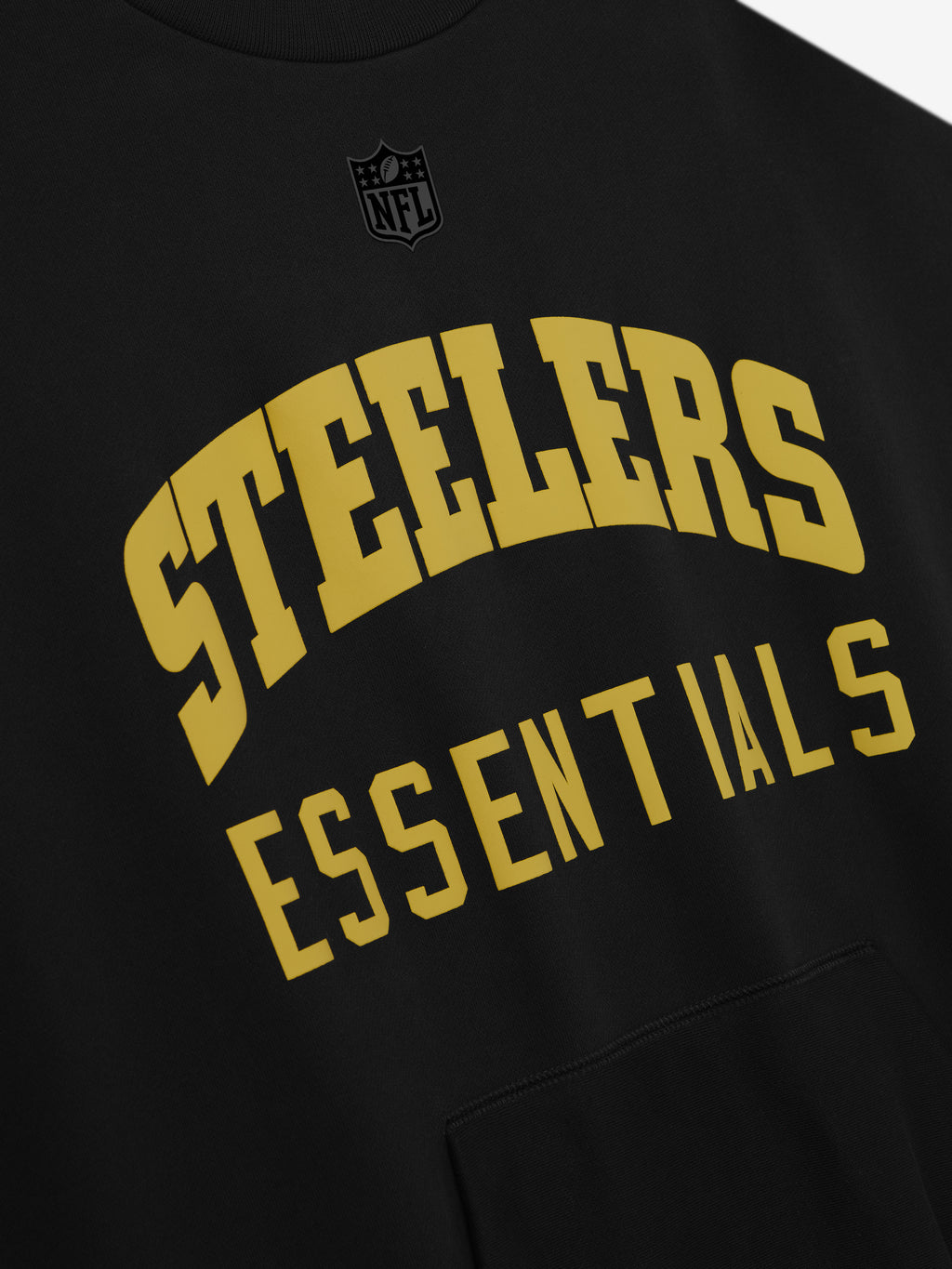 Close-up of black Steelers Sport Crewneck displaying large gold Steelers text and Essentials below with subtle NFL logo above chest