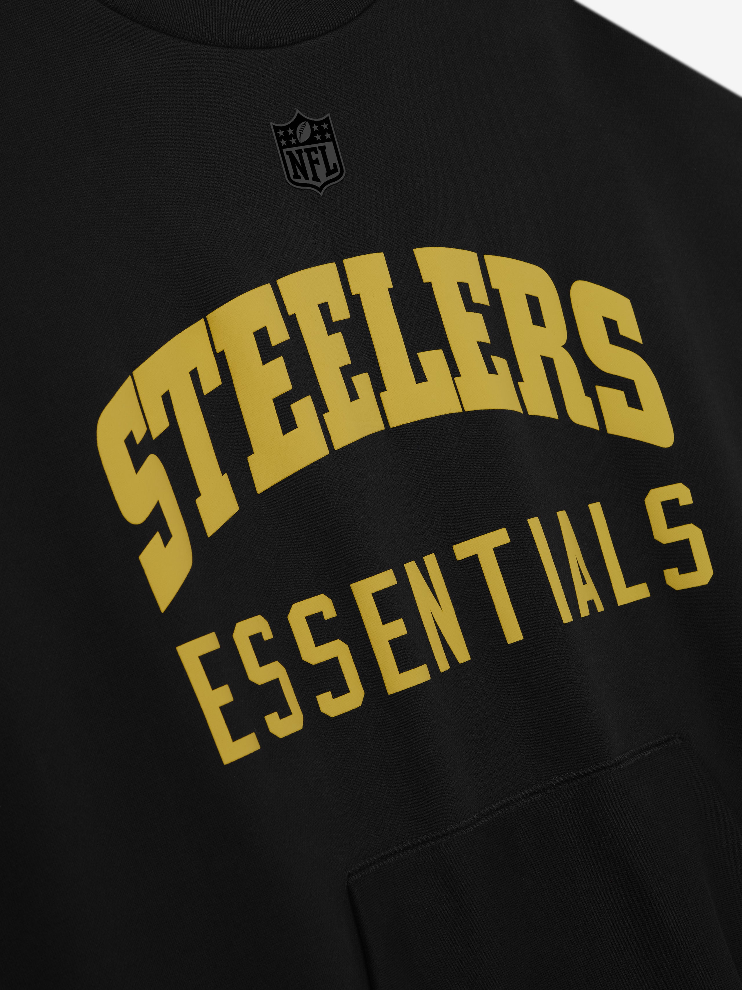 Close-up of black Steelers Sport Crewneck displaying large gold Steelers text and Essentials below with subtle NFL logo above chest