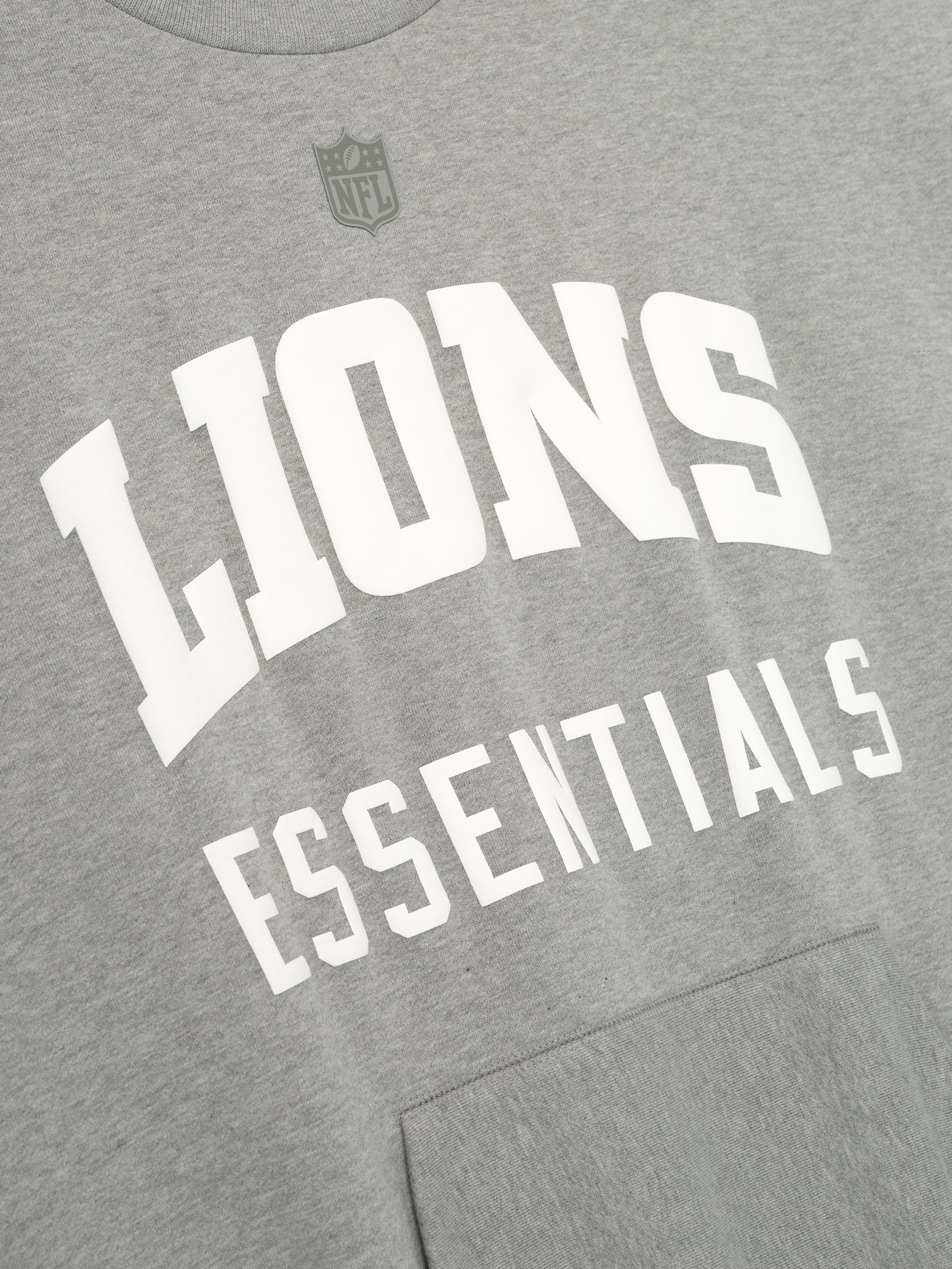 Close-up of concrete heather Lions Sport Crewneck showing bold white Lions Essentials text and subtle NFL shield above chest, gallery 0