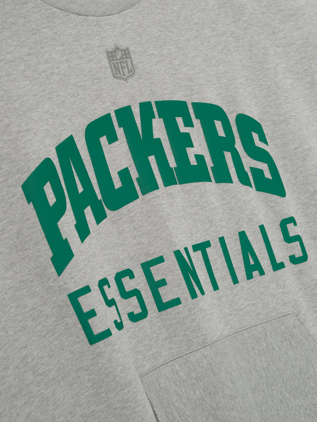Angled close-up of concrete heather Packers Sport Crewneck showing green Packers Essentials lettering with subtle NFL logo above chest