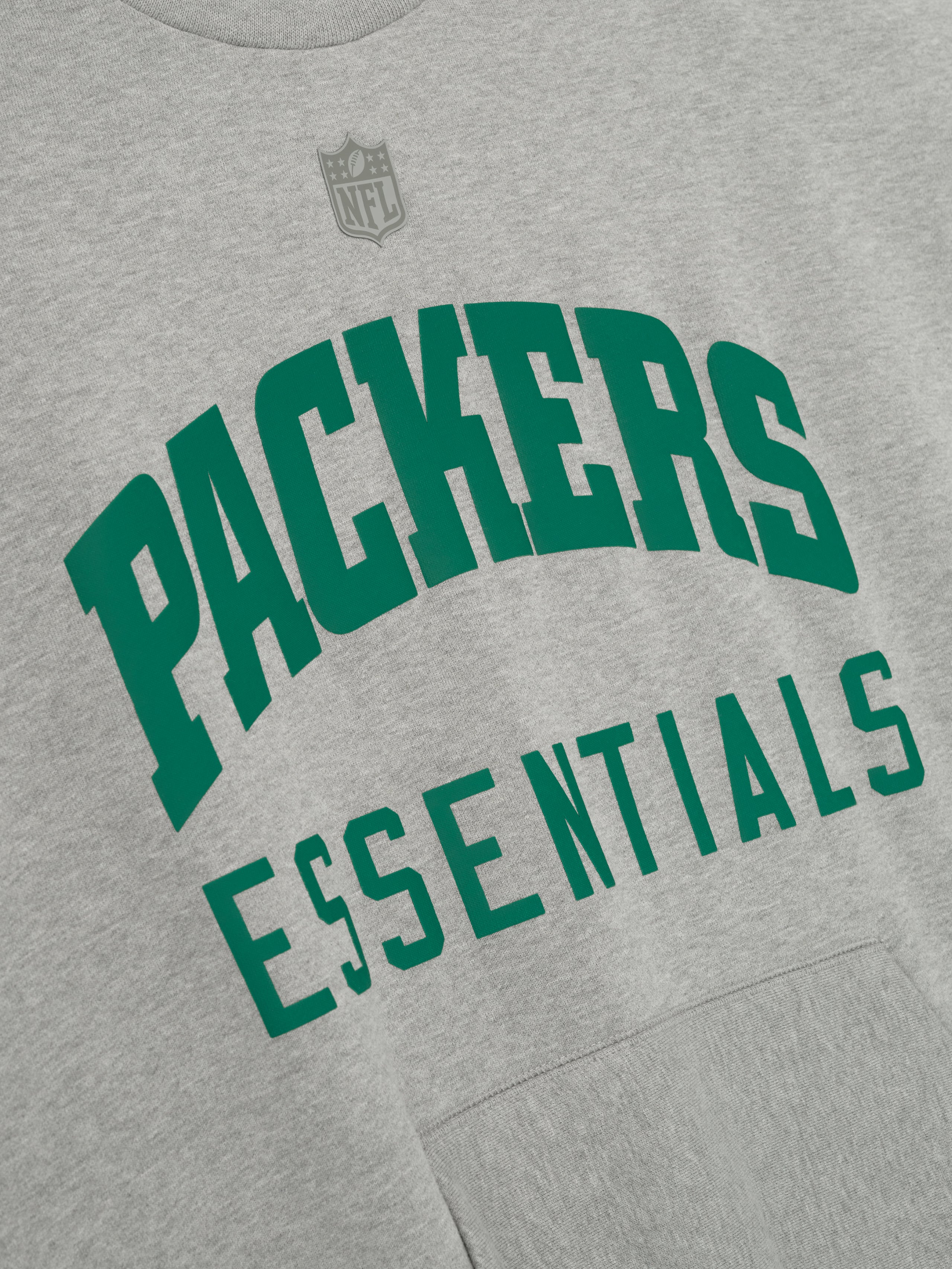Angled close-up of concrete heather Packers Sport Crewneck showing green Packers Essentials lettering with subtle NFL logo above chest