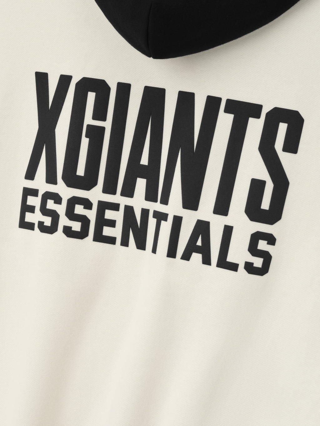 close-up of cream hoodie front with bold embossed black "XGIANTS ESSENTIALS" text and black hood visible above