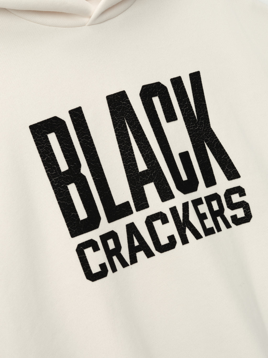 cream-colored hoodie close-up with textured black "BLACK CRACKERS" felt lettering on front panel