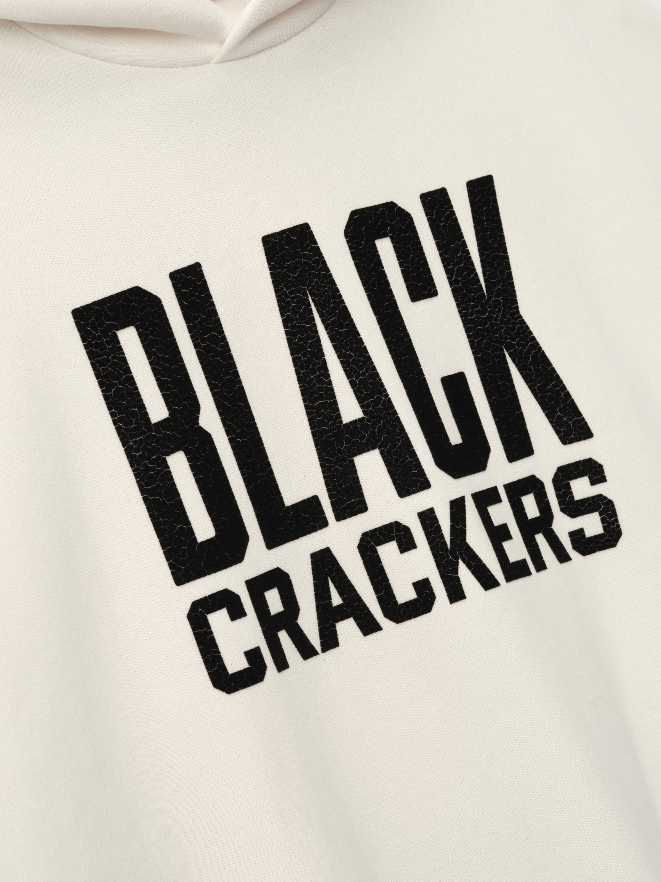 cream-colored hoodie close-up with textured black "BLACK CRACKERS" felt lettering on front panel