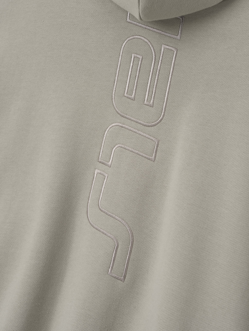 close-up of beige fleece fabric with raised stitched vertical Active Trace logo detail on hoodie back