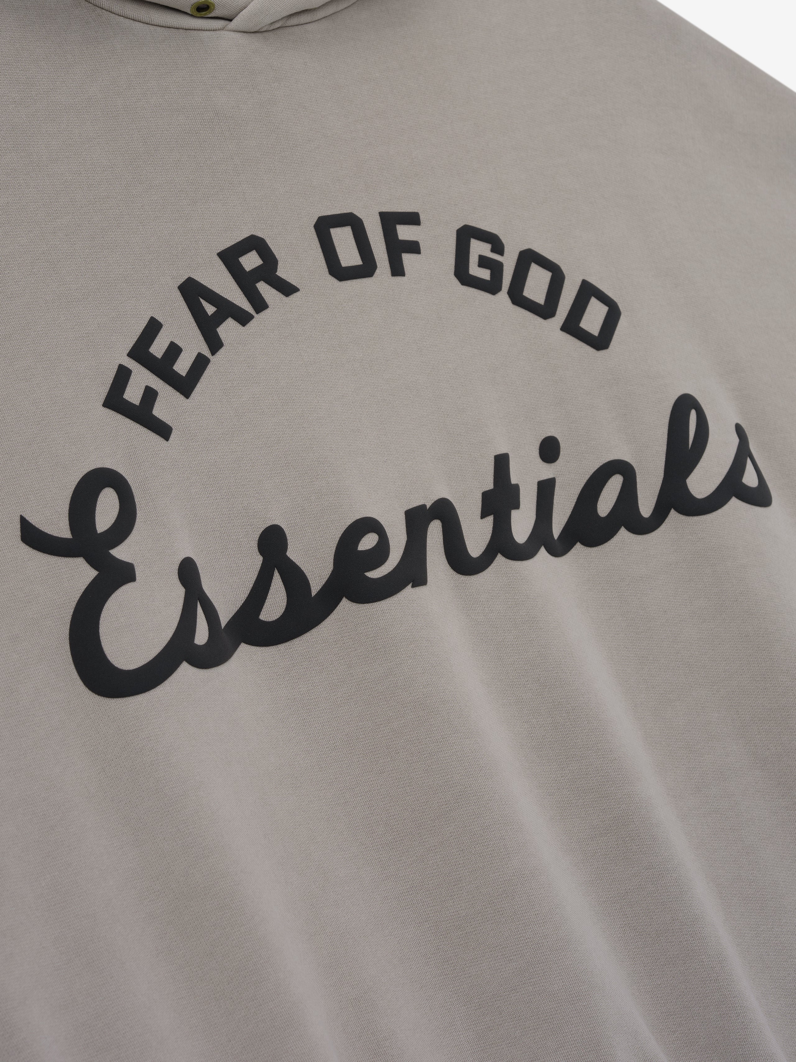 close-up of taupe cotton fleece hoodie with black puff-printed Fear of God Essentials logo on front