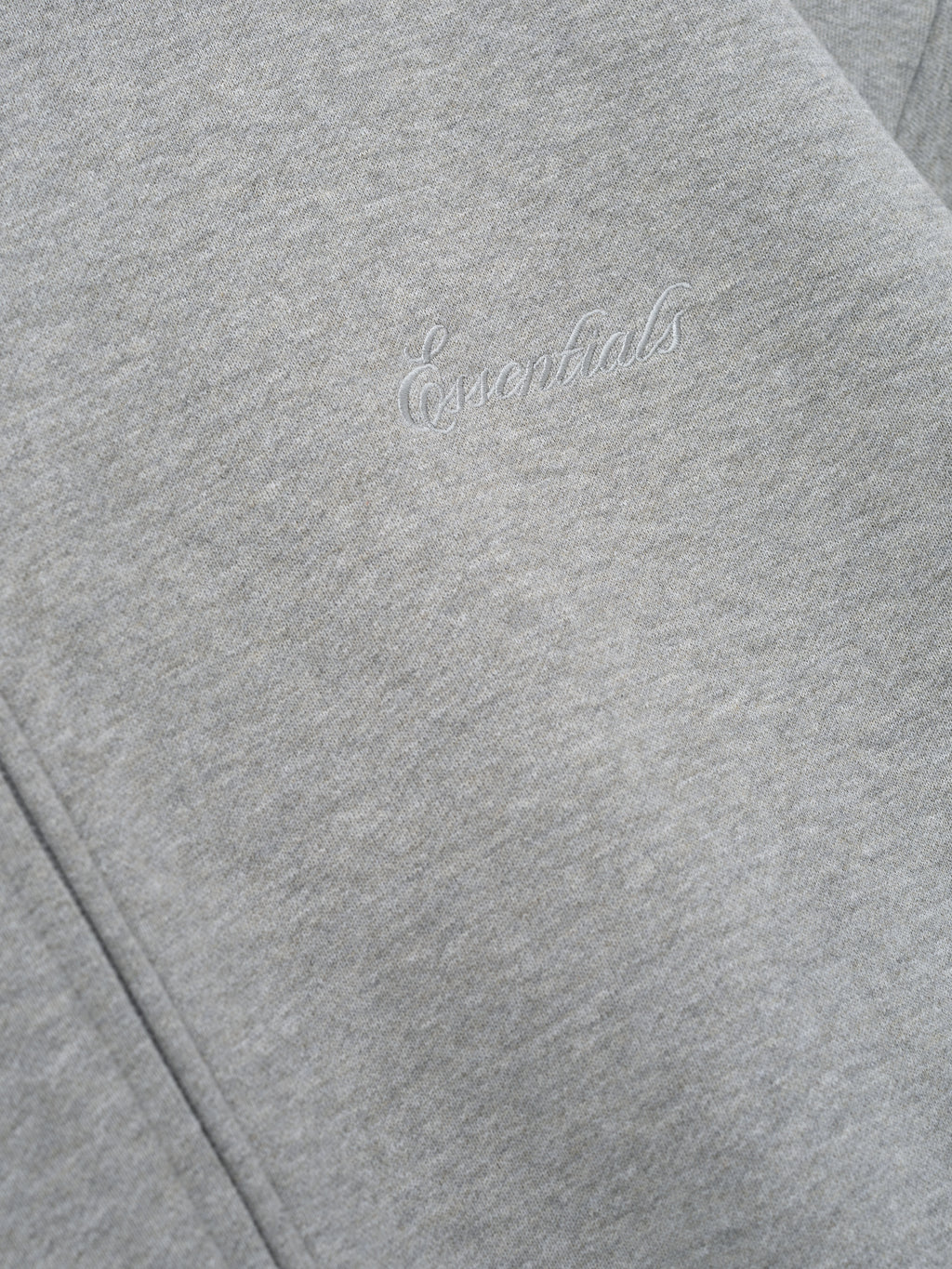 close-up of light gray core fleece hoodie with stitched Essentials signature logo on front panel near zipper