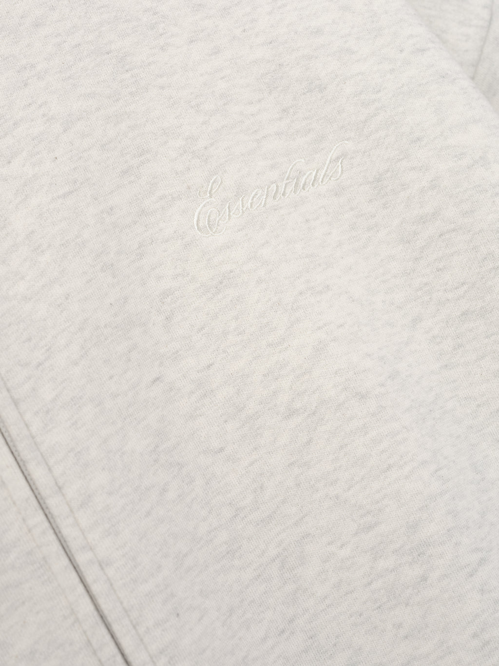 close-up of light gray core fleece fabric with white embroidered Essentials signature logo on front panel