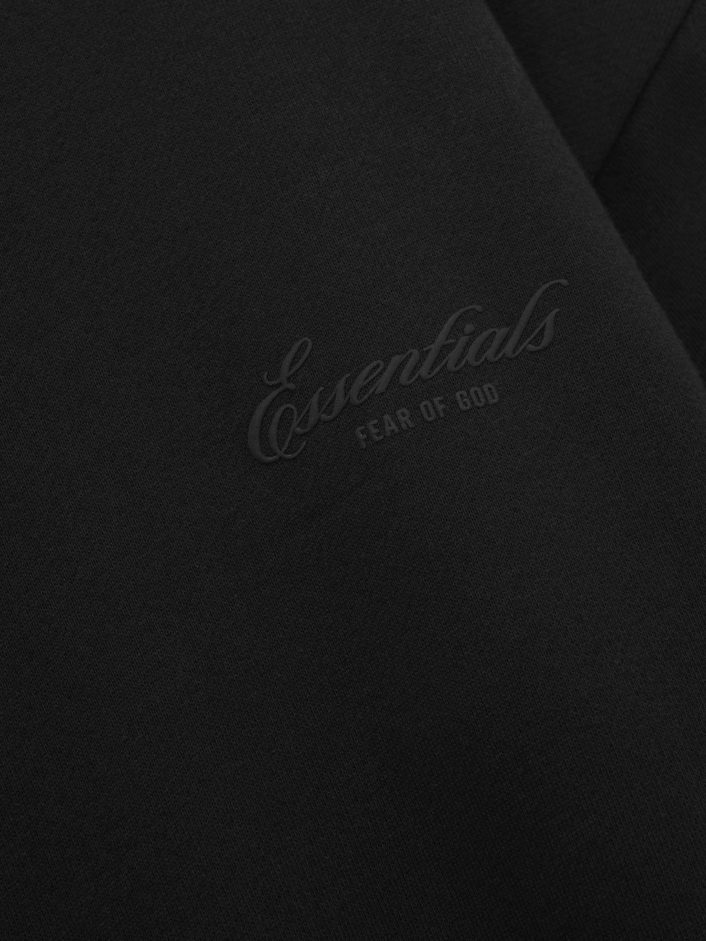 close-up of black fleece fabric with embossed Essentials Fear of God logo on chest panel of sweatshirt