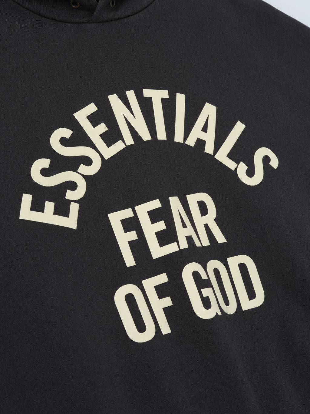 close-up of black pigment-dyed hoodie with cream Essentials Fear of God arched logo print on chest