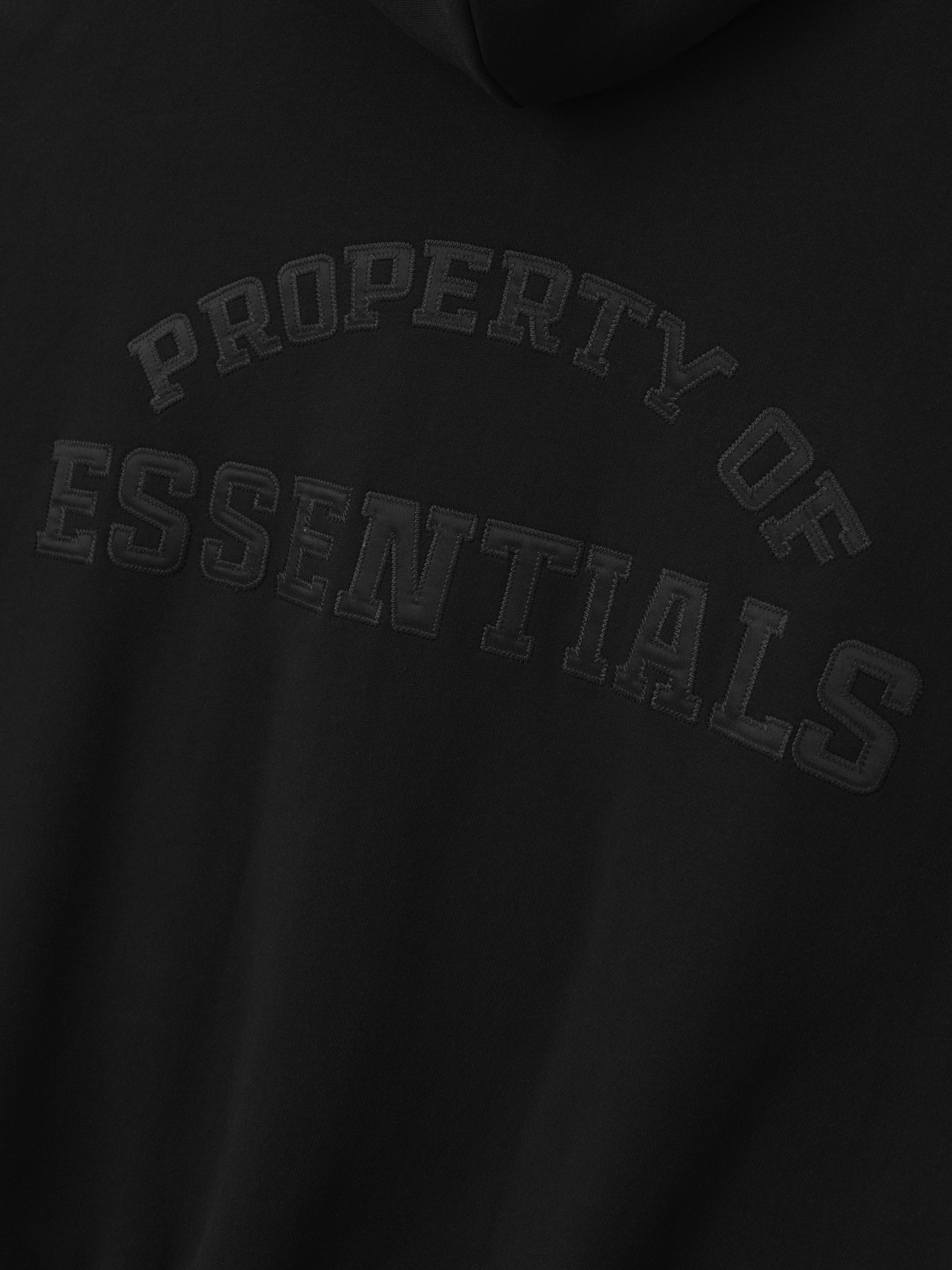 Close-up of black hoodie with raised textured text "Property of Essentials" on the chest area