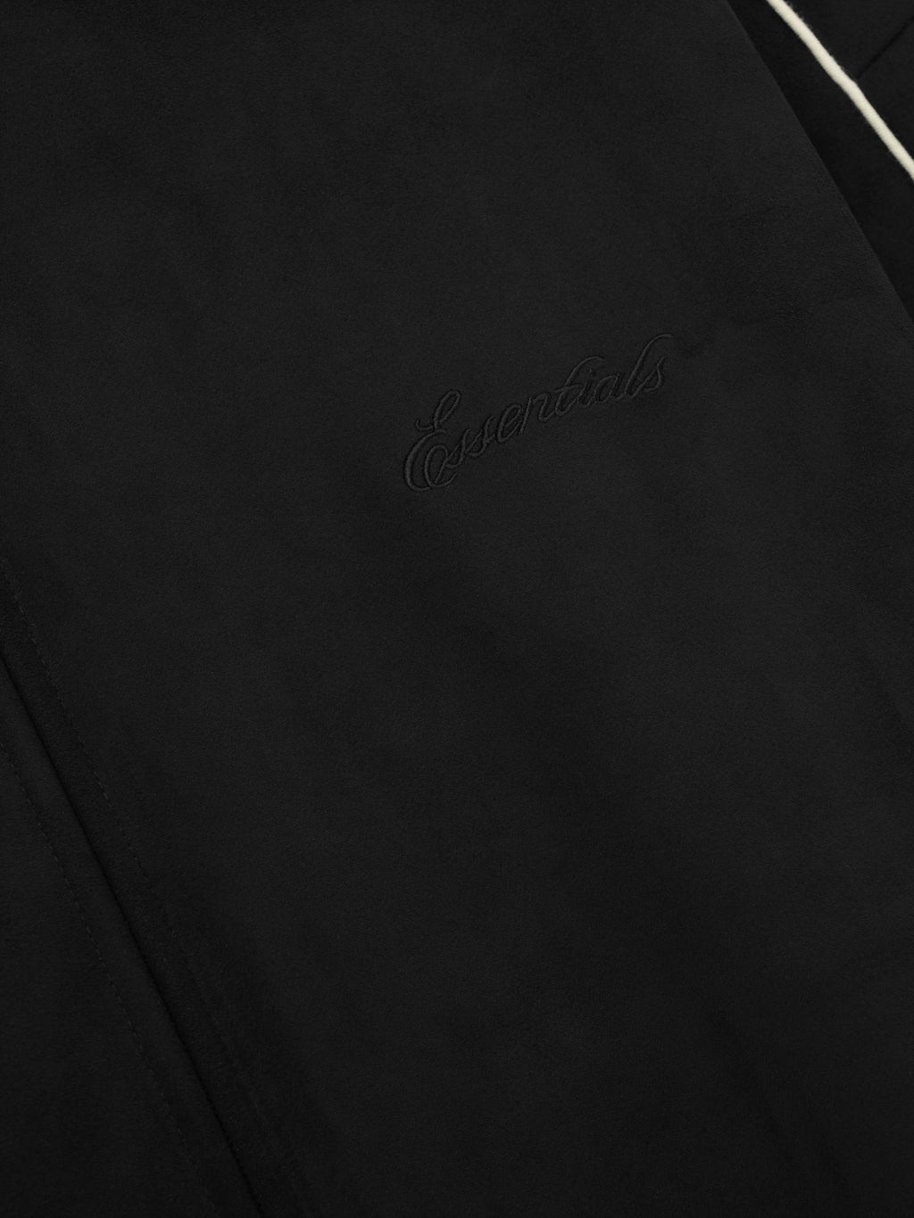 close-up of black bonded suede fleece fabric with subtle embossed Essentials logo and white piping detail