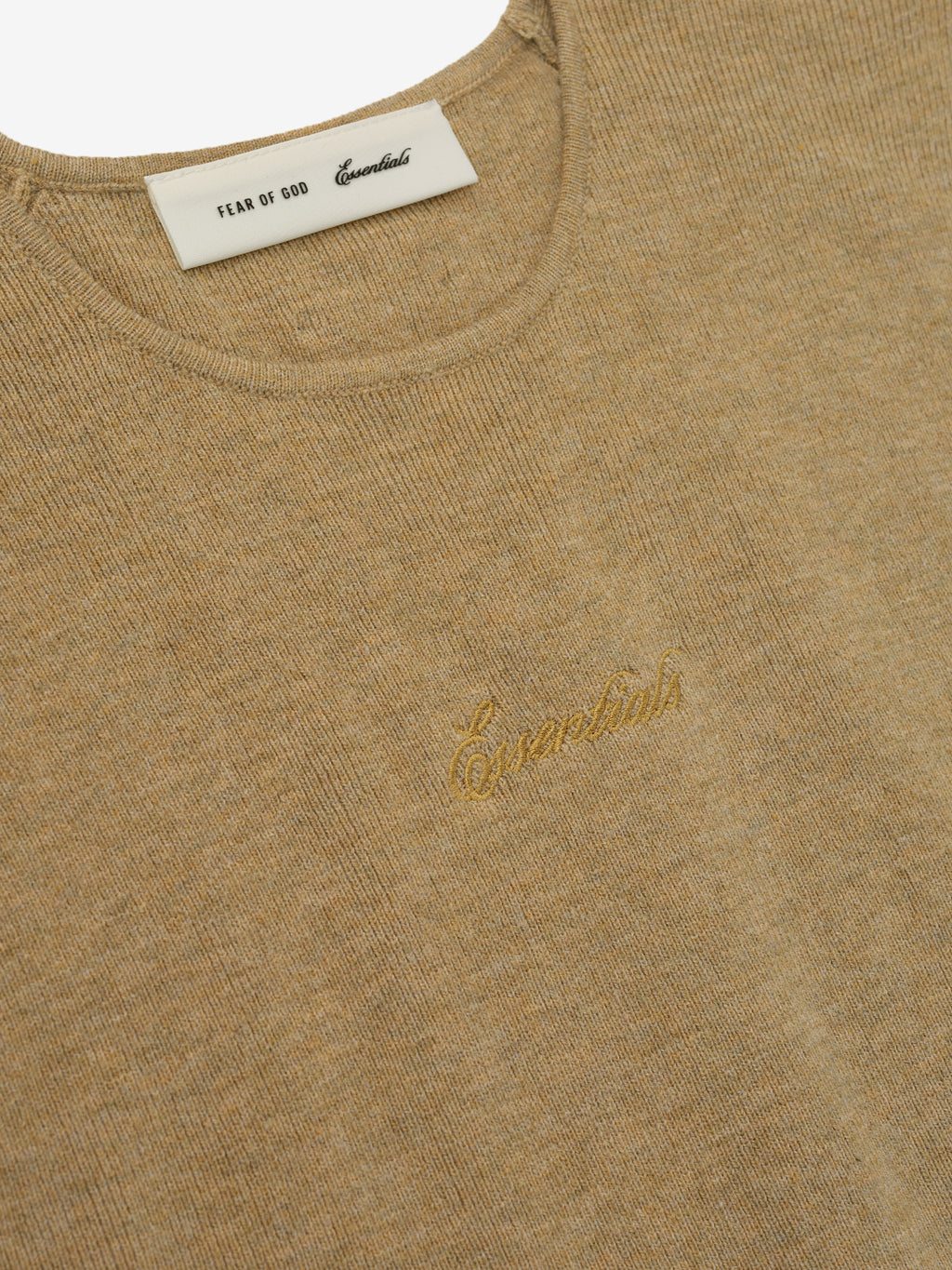 Close-up of a beige sweater with a gold logo and label on a white background