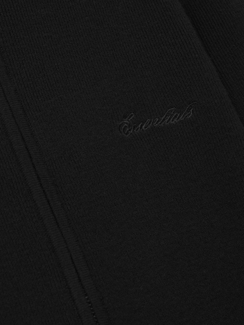 Close-up of a black fabric with 'Essentials' embroidery on a dark background