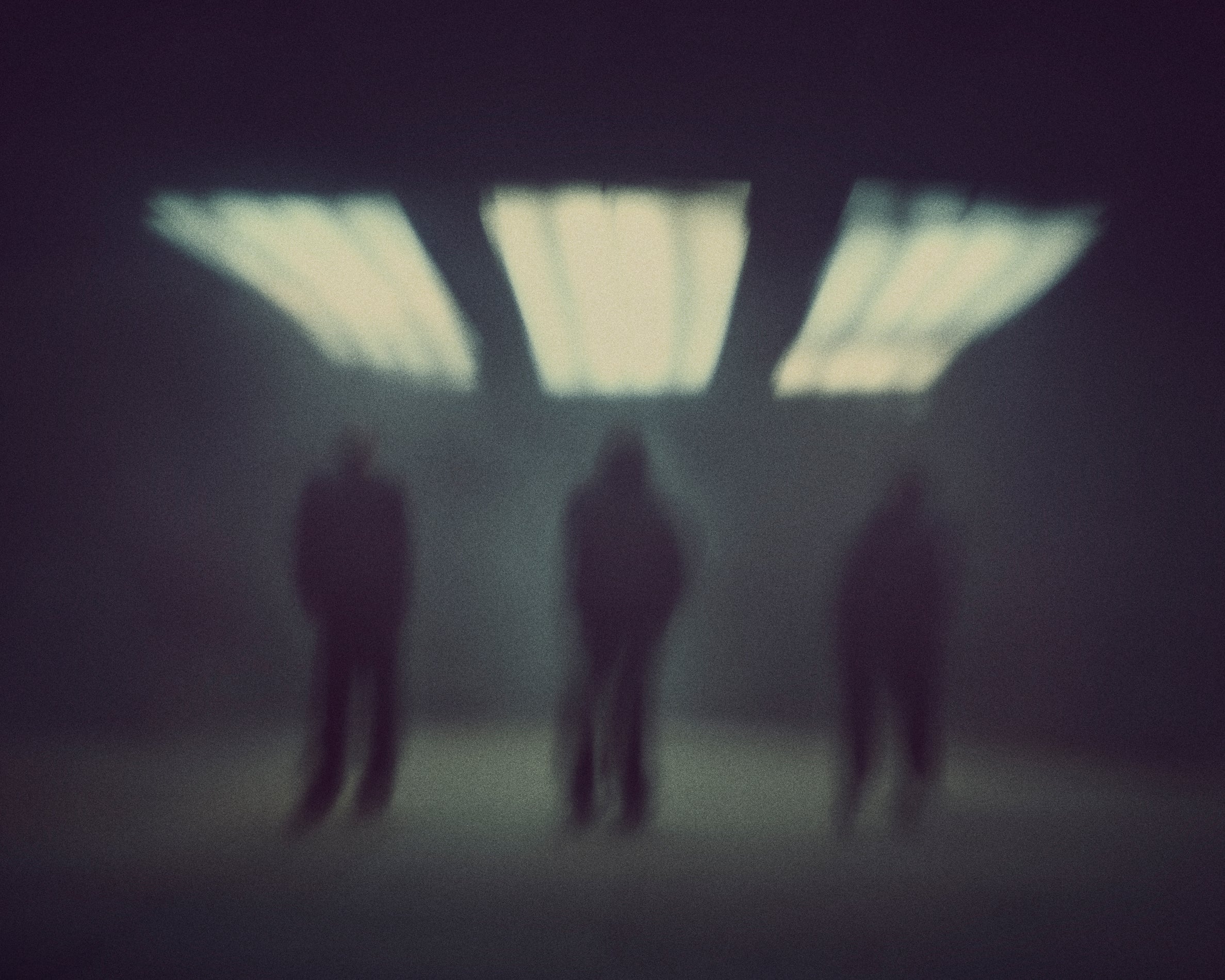 Three indistinct human figures standing under bright rectangular lights in a dark, blurry environment