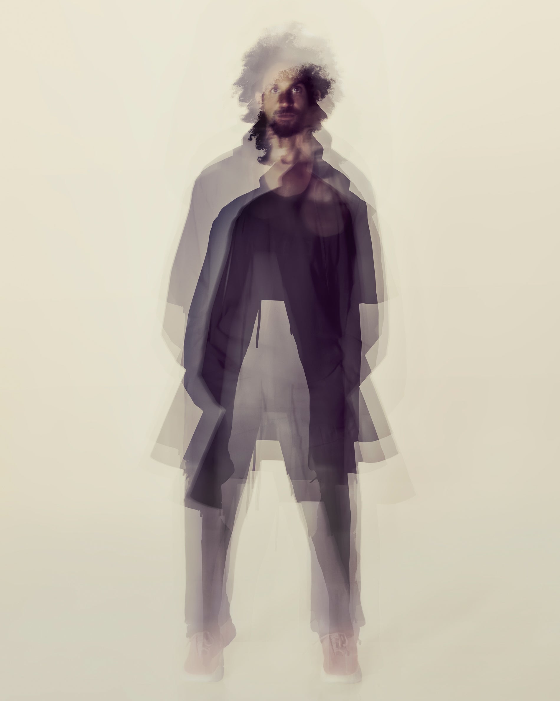 Blurred double exposure of a man with curly hair wearing dark casual clothing on a light background
