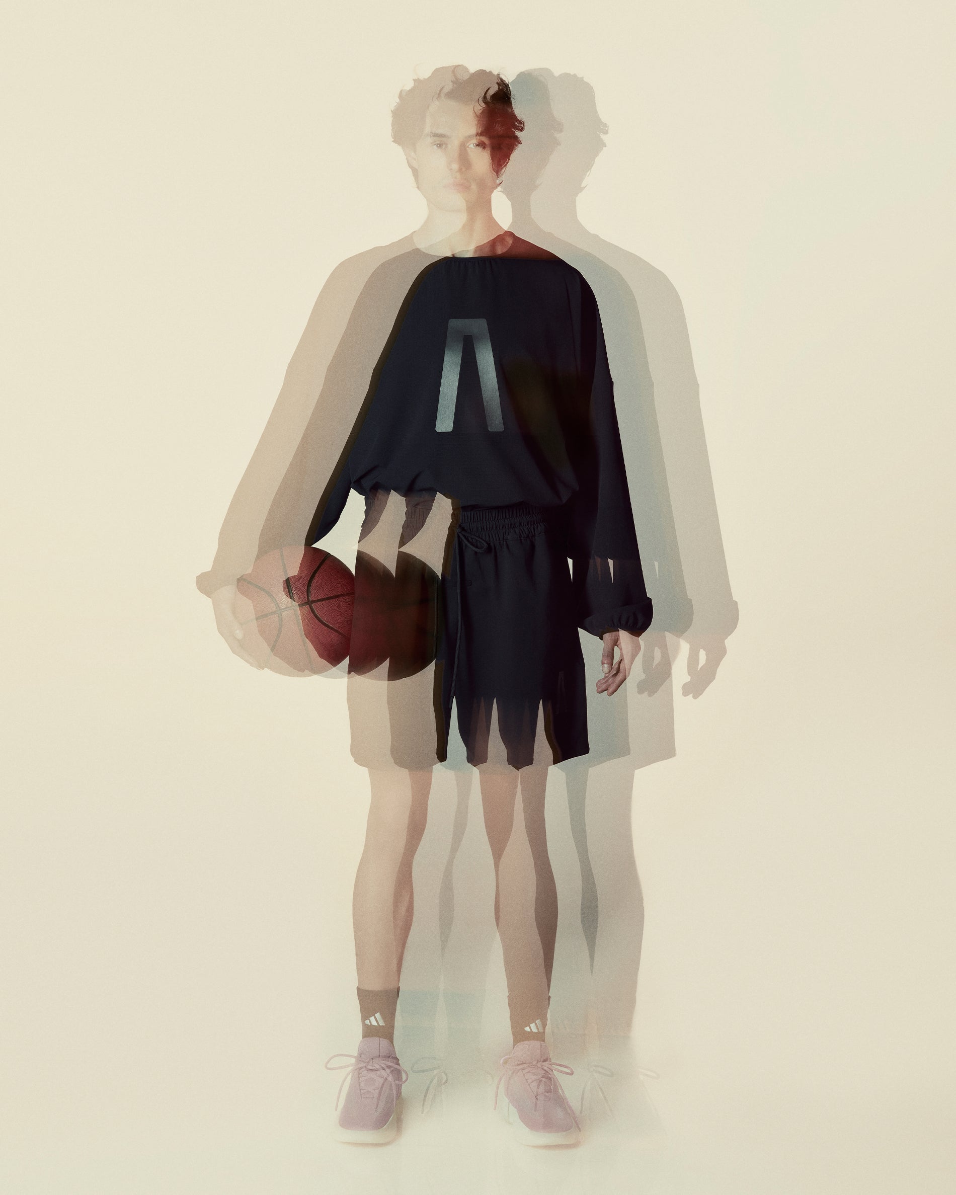 Young person in dark athletic wear holding a basketball with a blurred multiple exposure effect on a pale background