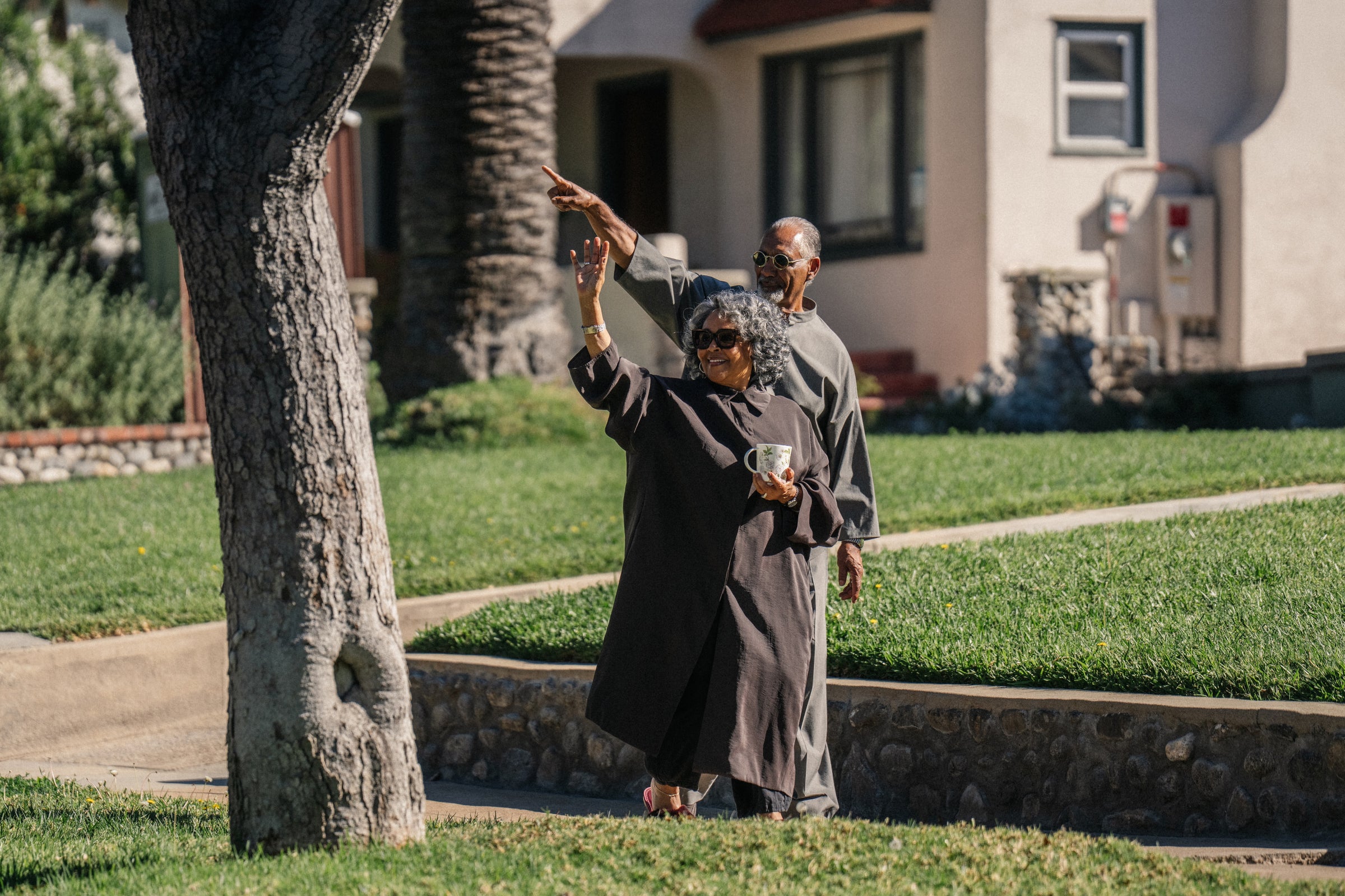 Older couple standing on sidewalk with the woman pointing ahead while holding a cup in a residential neighborhood
