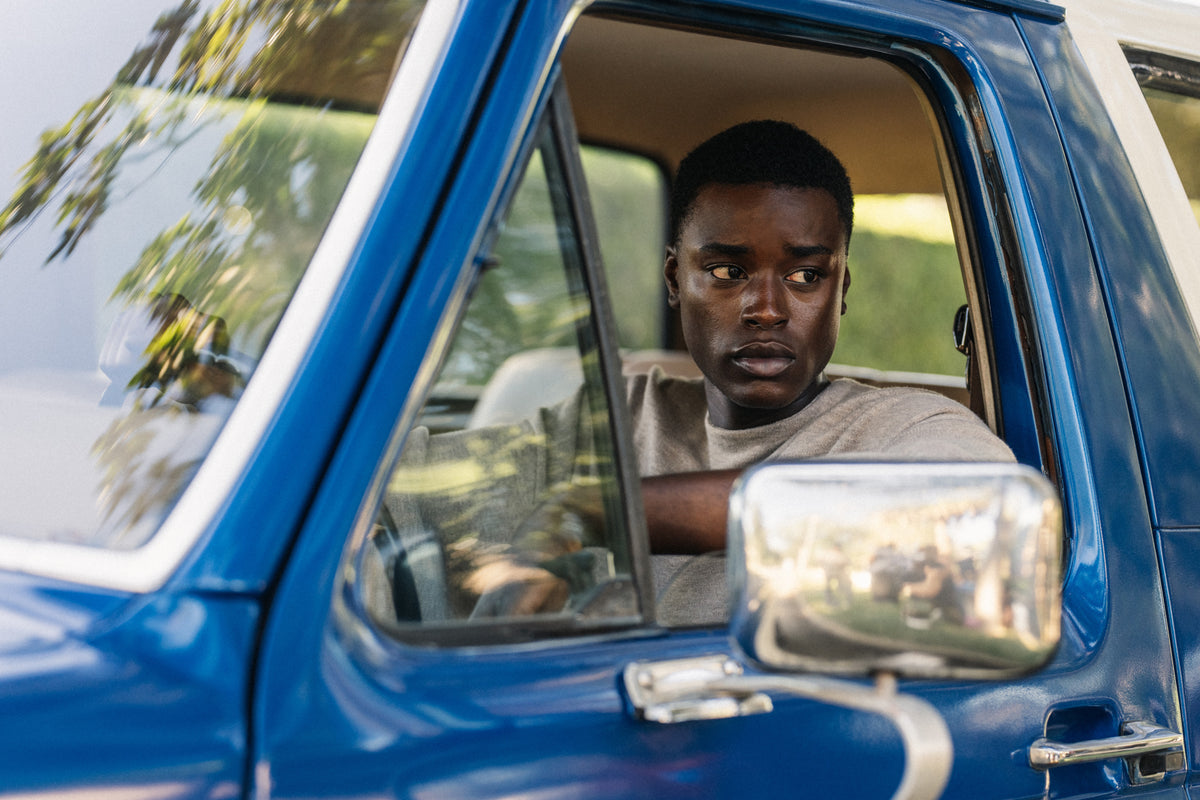 Young man in light gray shirt looking to the side while sitting inside a blue vintage vehicle with window rolled down