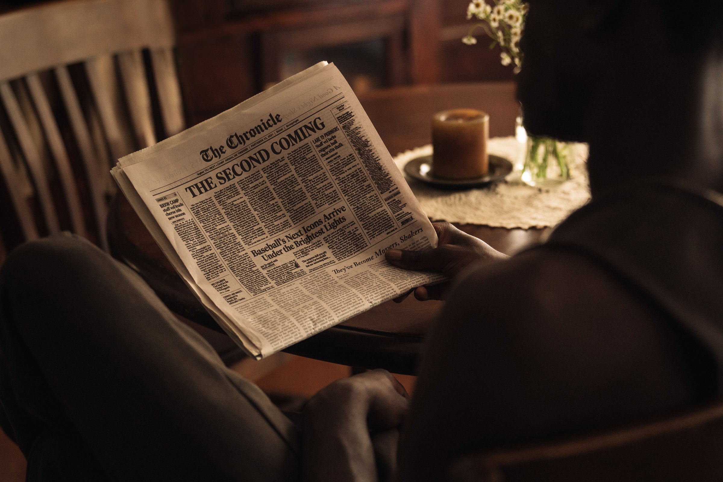 Person sitting in wooden chair reading a newspaper titled 