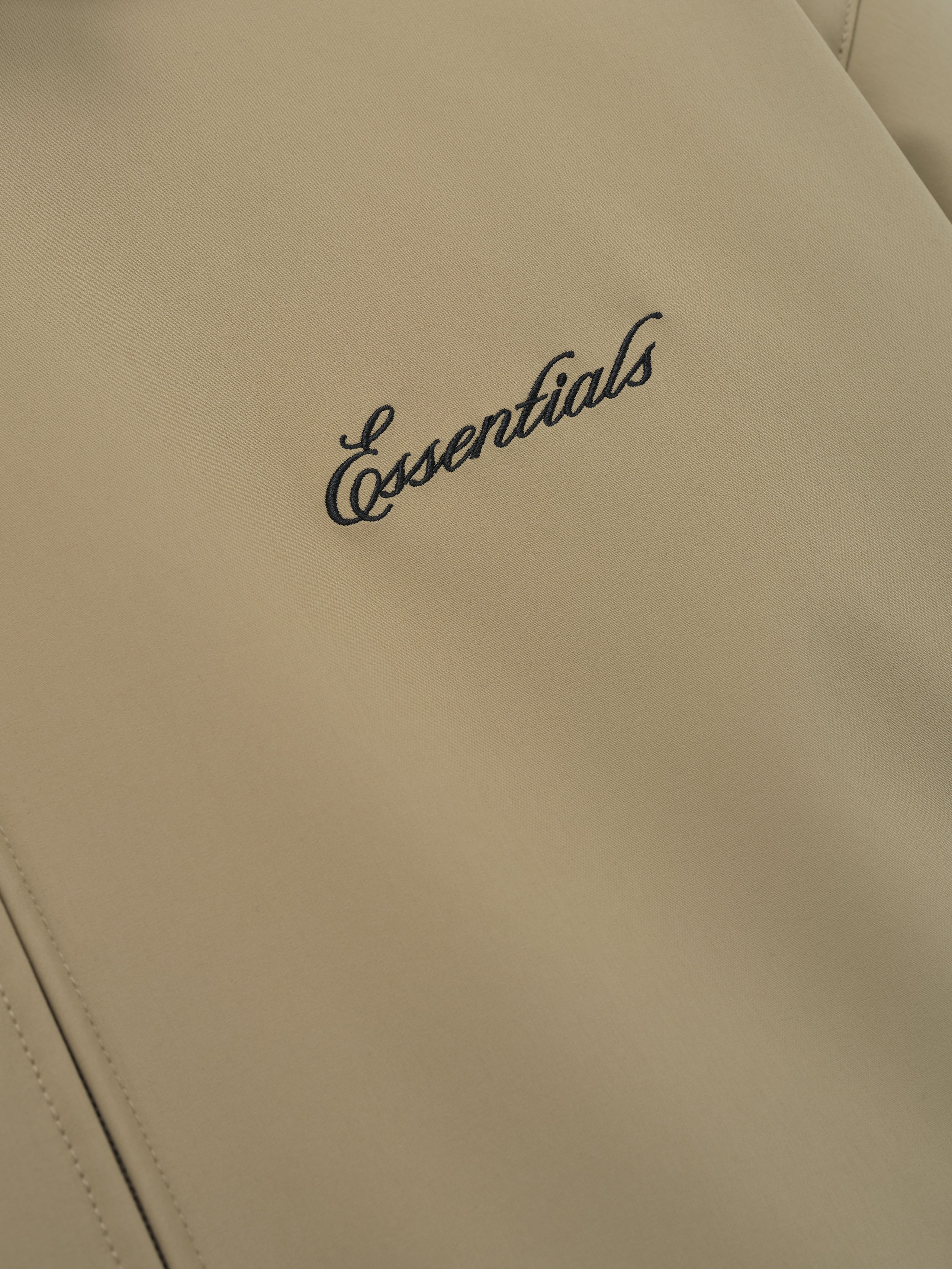 close-up of beige bonded nylon fabric with black Essentials logo embroidered on Signature Filled Barn Jacket