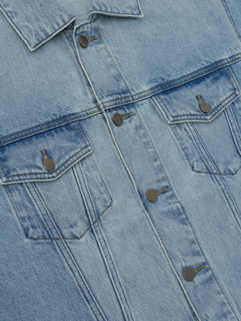 Close-up of light wash denim jacket front with button closures and two flap chest pockets on light background