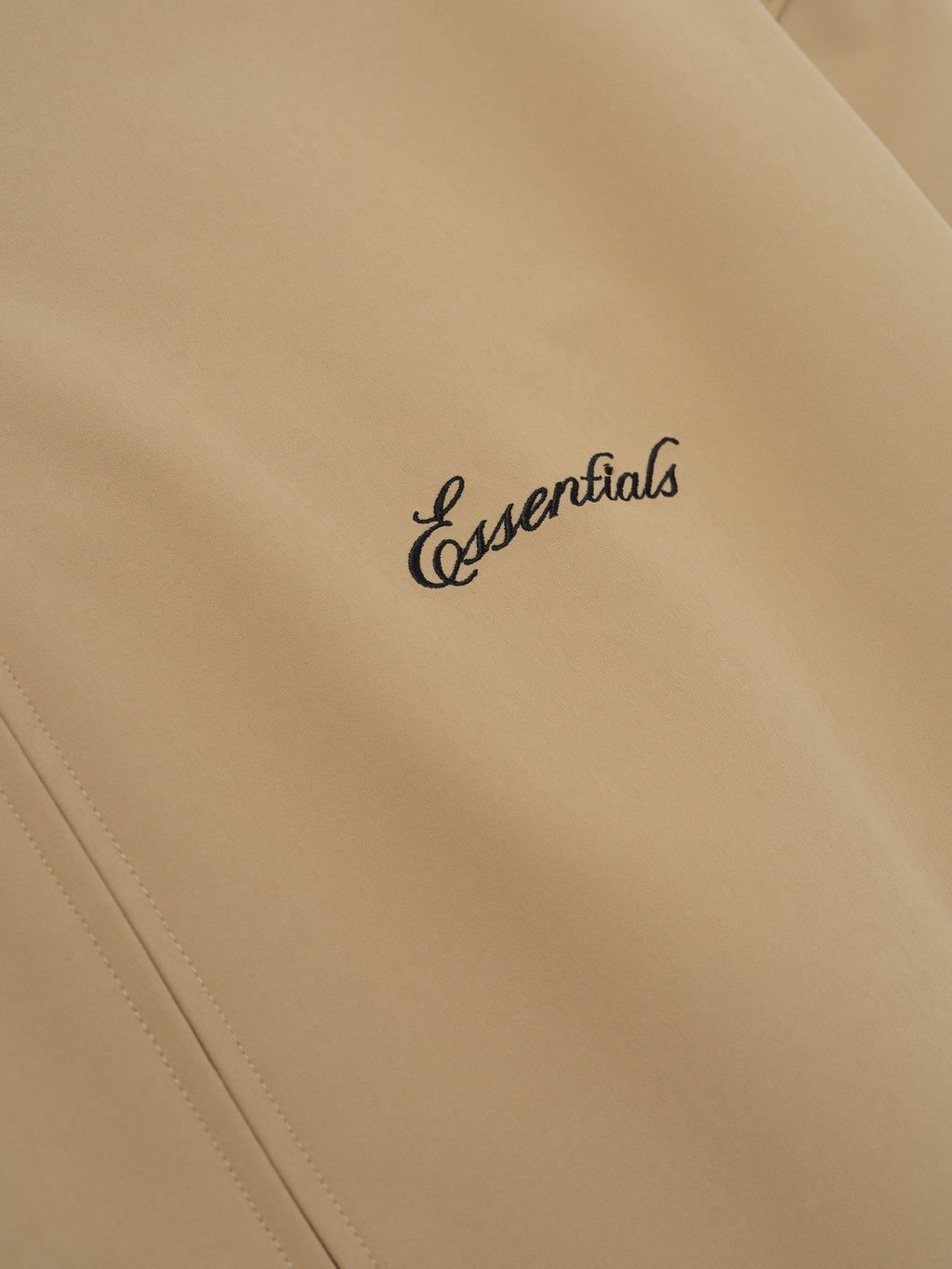 Beige jacket with 'essentials' embroidery on a beige background