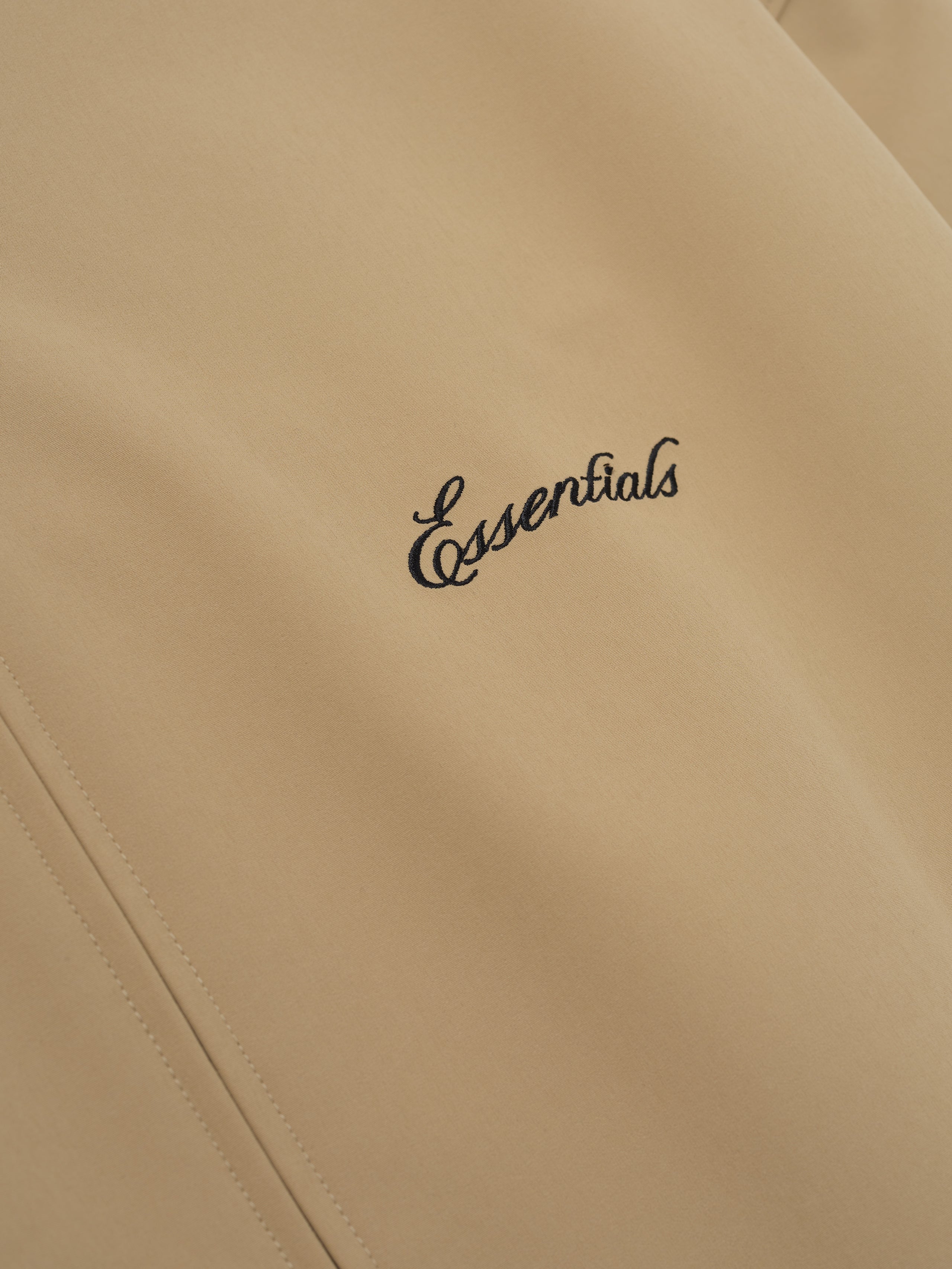 Beige jacket with 'essentials' embroidery on a beige background