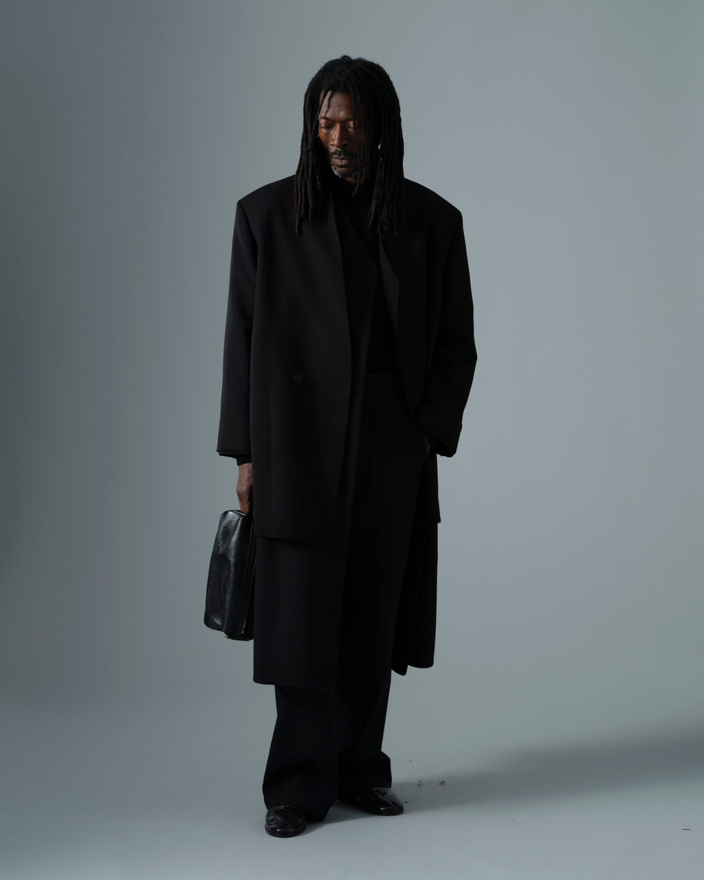 Easy Care Wool Lapelless Mid-length Jacket worn in black with a relaxed silhouette and long sleeves styled with black trousers and a leather bag as Outerwear