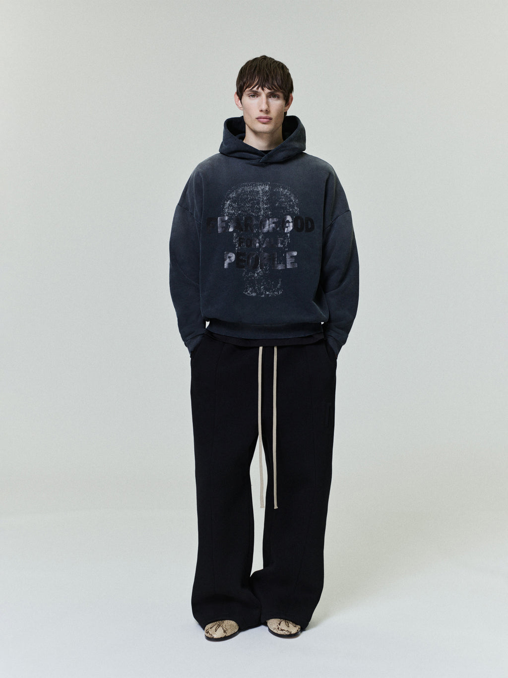 Le Panteres Hoodie in faded black featuring a textured graphic print and subtle lettering, styled with loose black trousers for a contemporary casual outerwear look.