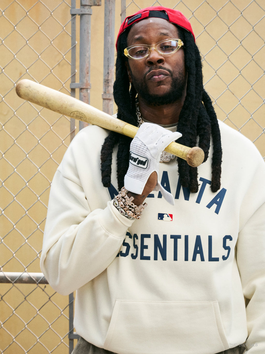 Cream Braves Sport crewneck with navy blue "ATLANTA ESSENTIALS" text worn by man holding baseball bat over shoulder