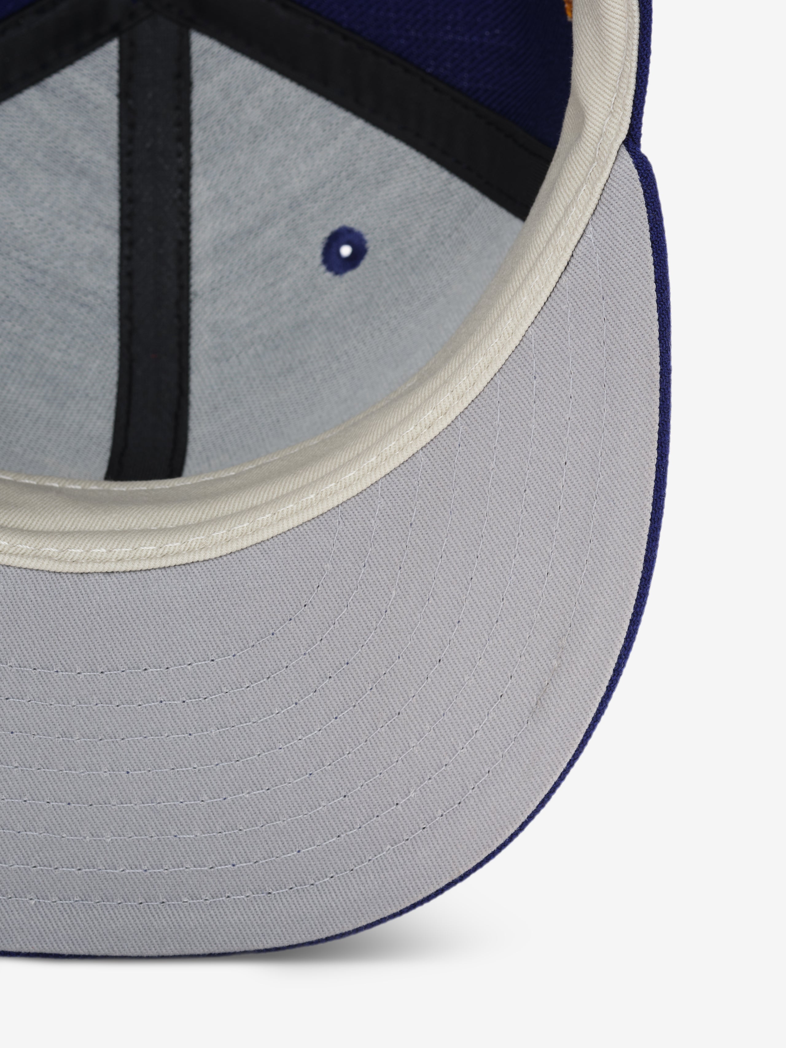 Close-up of the inner brim of a blue baseball cap showing light gray fabric and cream-colored trim with black stitching detail.