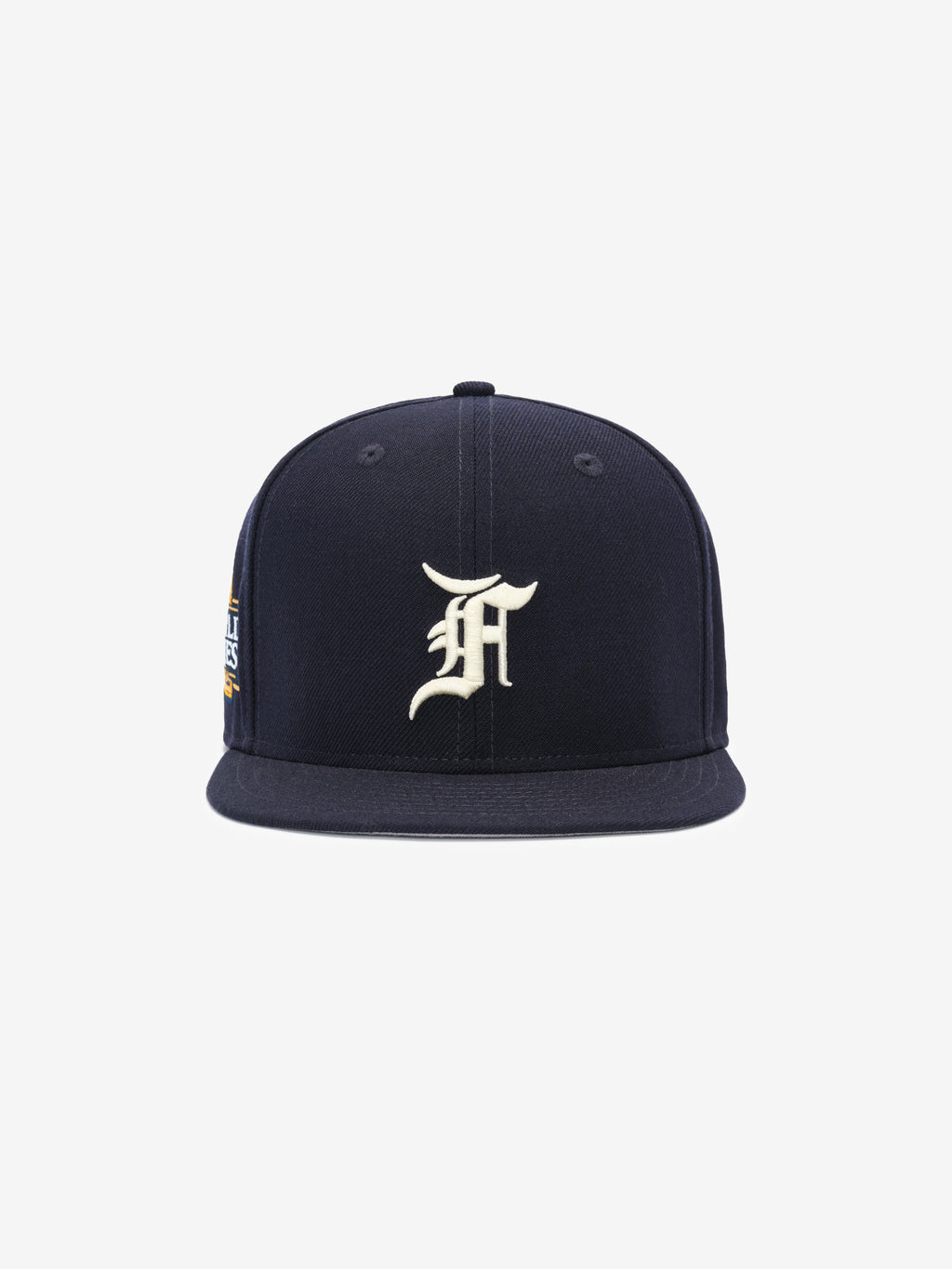 Front view of a navy blue structured snapback cap with a white ornate letter embroidered on the front panel