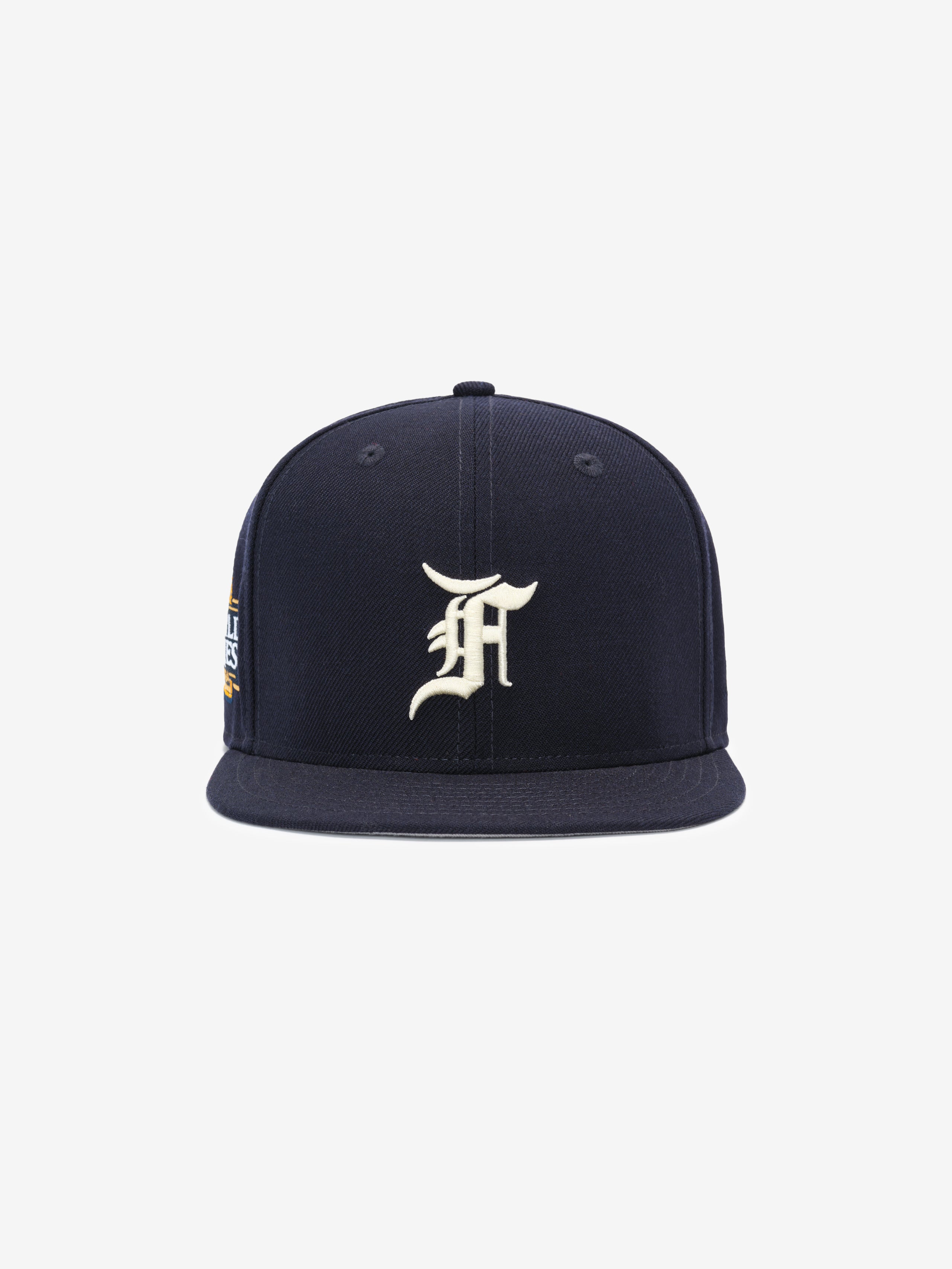 Front view of a navy blue structured snapback cap with a white ornate letter embroidered on the front panel