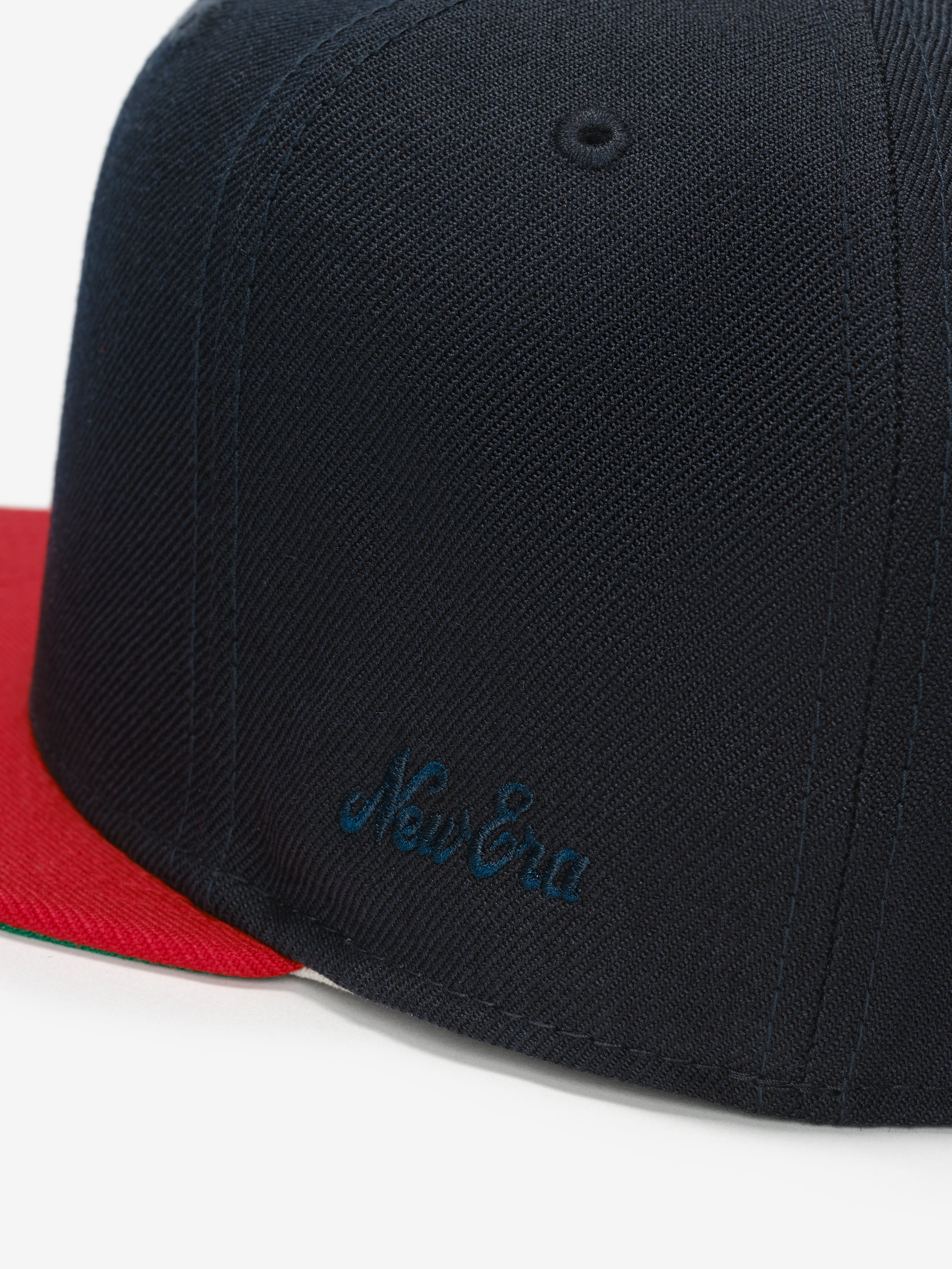 Fear of God Essentials 59FIFTY Athletics Cap featuring a navy textured crown with subtle tonal embroidery on the side and a contrasting vibrant red flat brim.