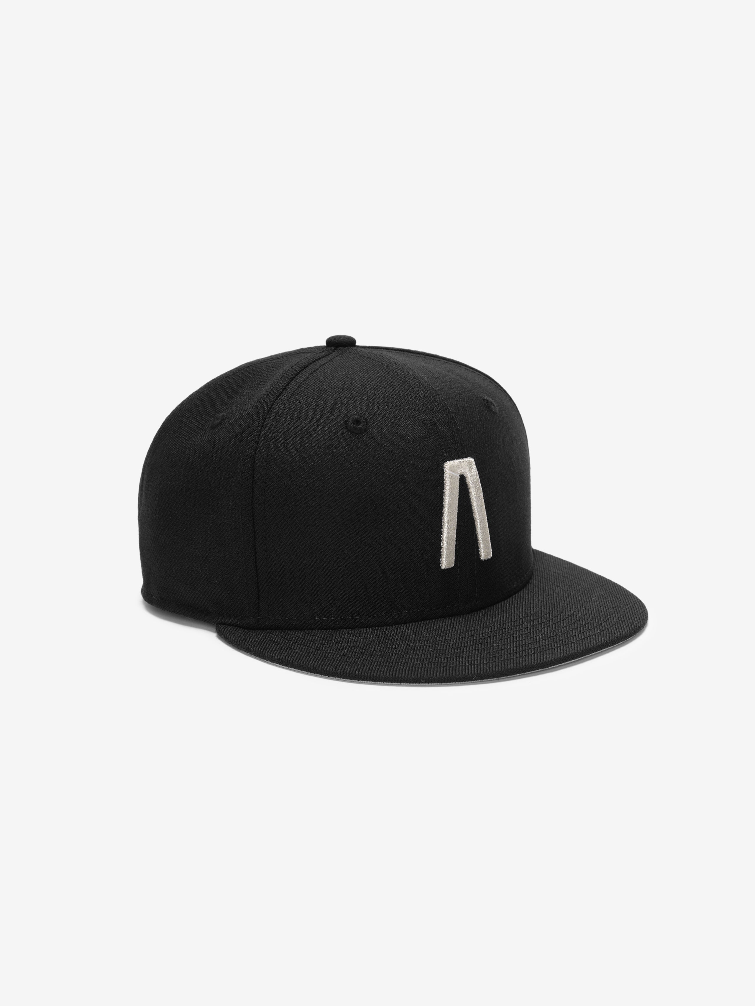 Fear of God Essentials 59FIFTY Athletics Cap featuring a solid black crown with a distinctive raised silver emblem on the front panel and a matching black flat brim.