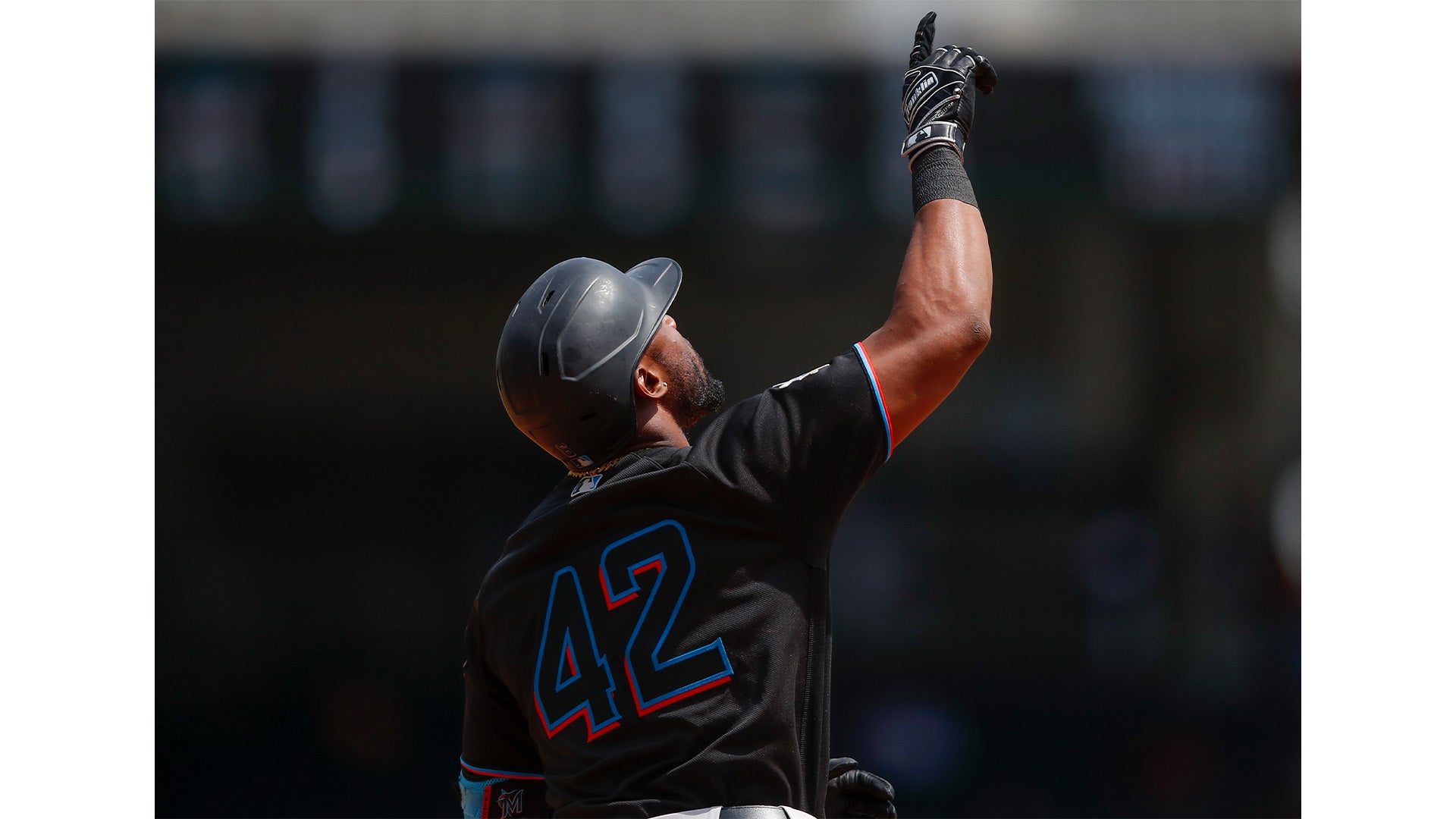 A baseball player wearing a black helmet and jersey number 42 points upward with his right hand while standing on the field during a game.