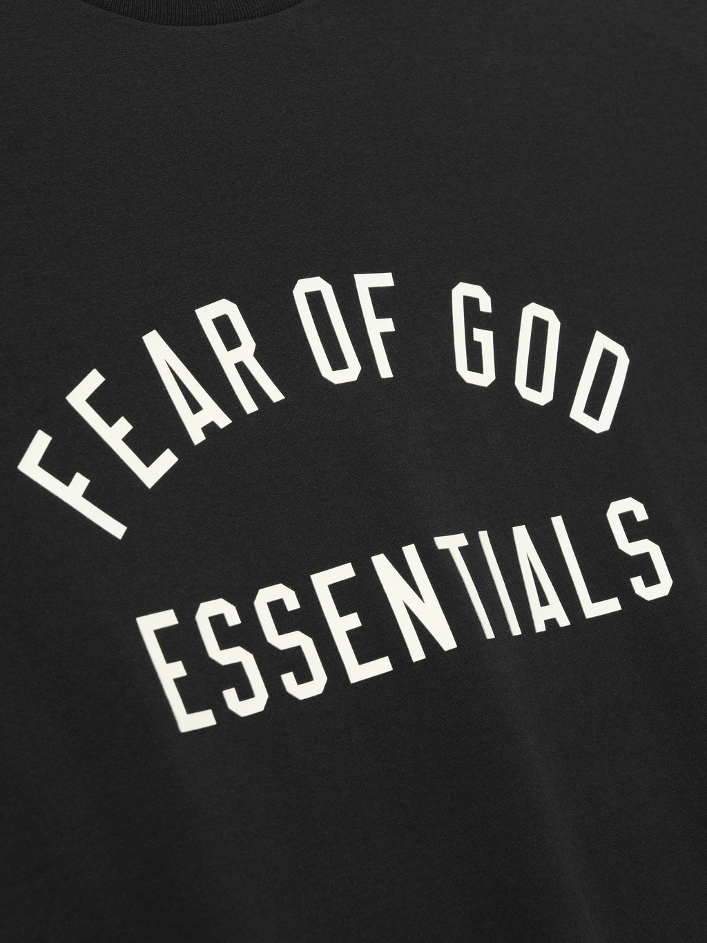 Close-up of black fabric with white "FEAR OF GOD ESSENTIALS" text printed in arched design on front panel