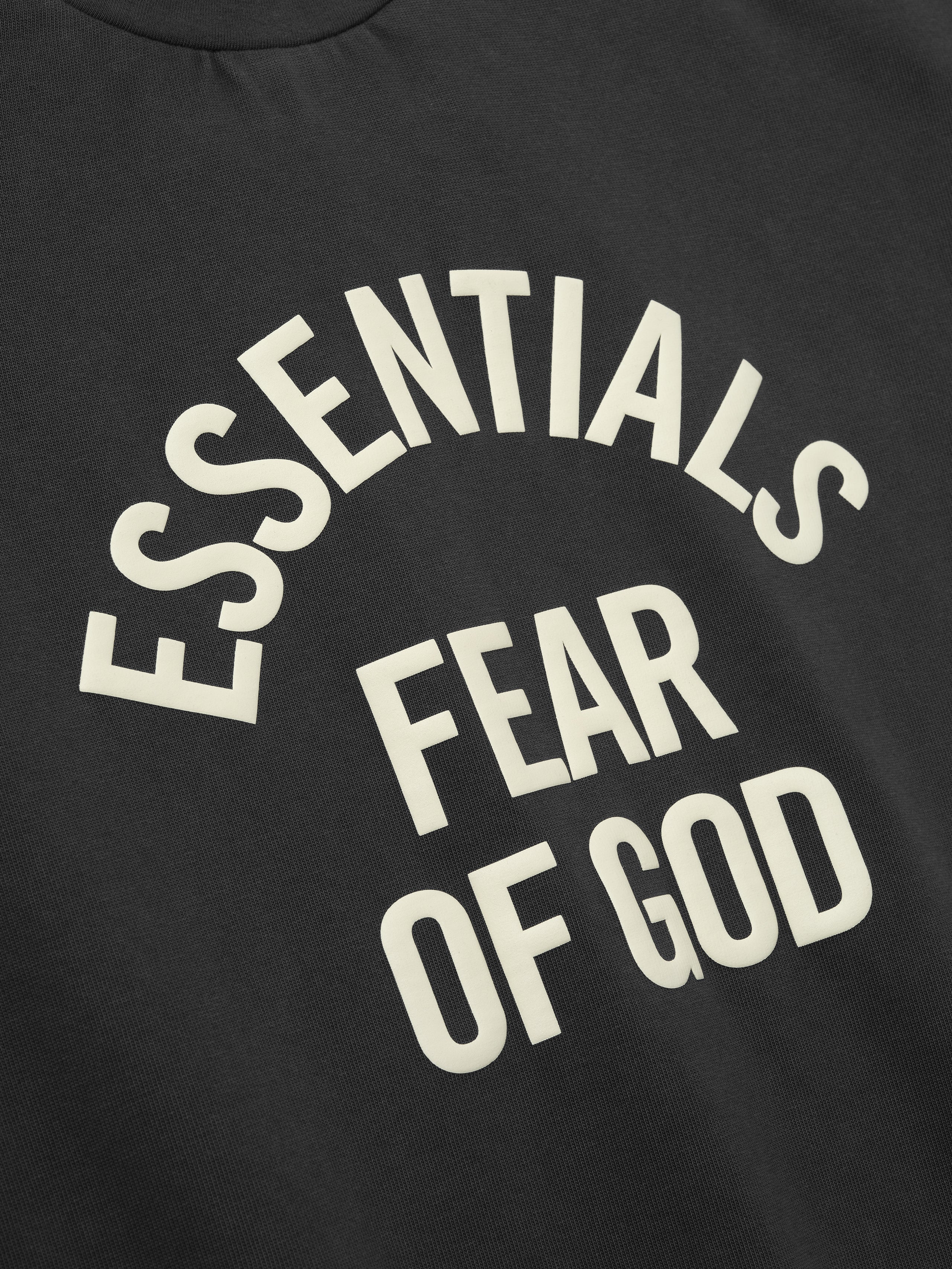 close-up of cream Essentials Fear of God logo arched over center on black heavyweight cotton jersey fabric