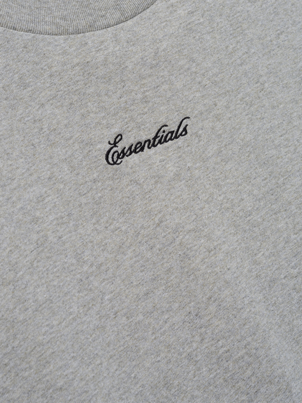 Close-up of the Kids Signature 90s Tee in soft concrete heather fabric featuring black cursive Essentials embroidery on the chest for a casual, classic look.